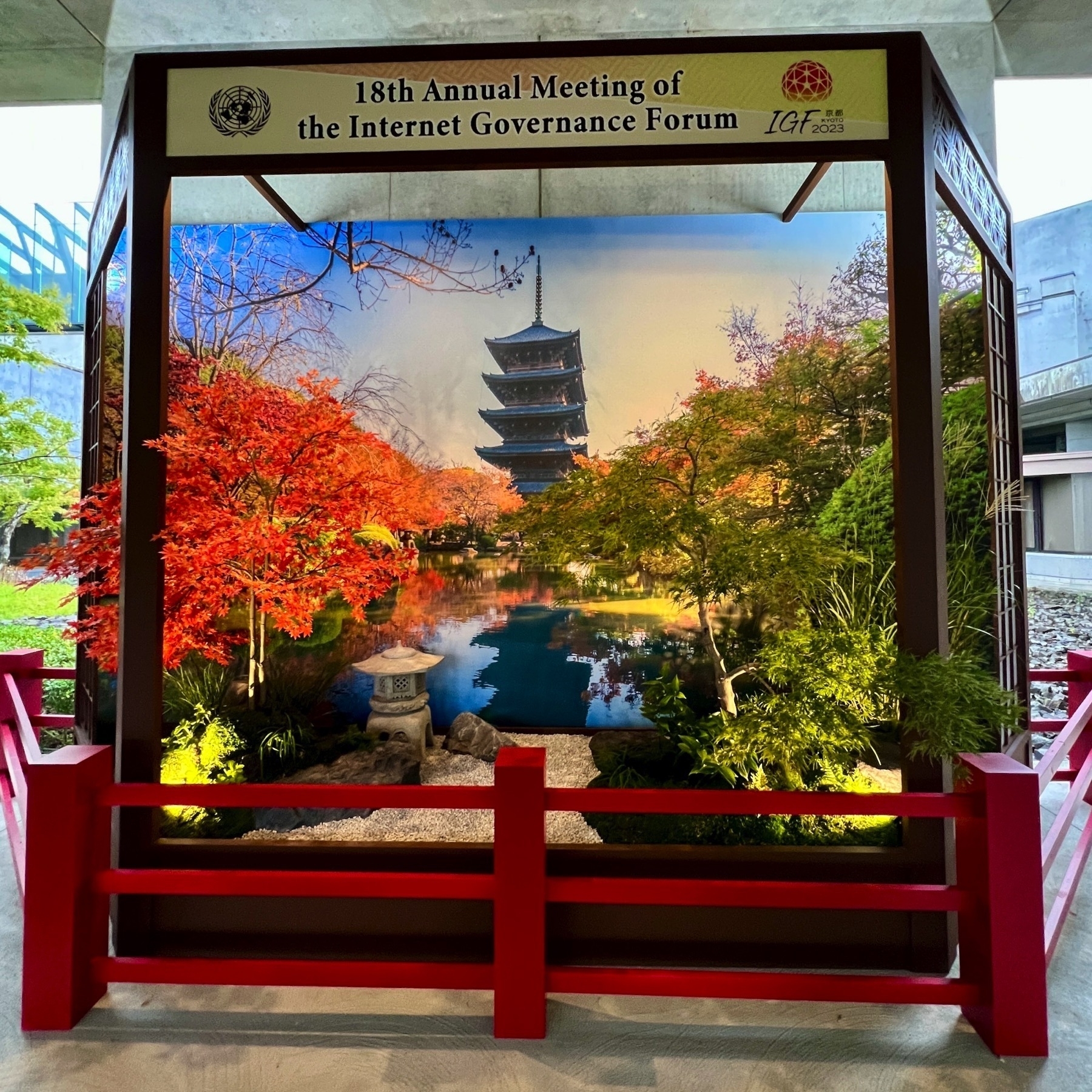 Display with two maple trees, one green and one turned red with the season. In the background is a picture of the Toji pagoda, above is a sign for the 18th Annual Meeting of the Internet Governance Forum.