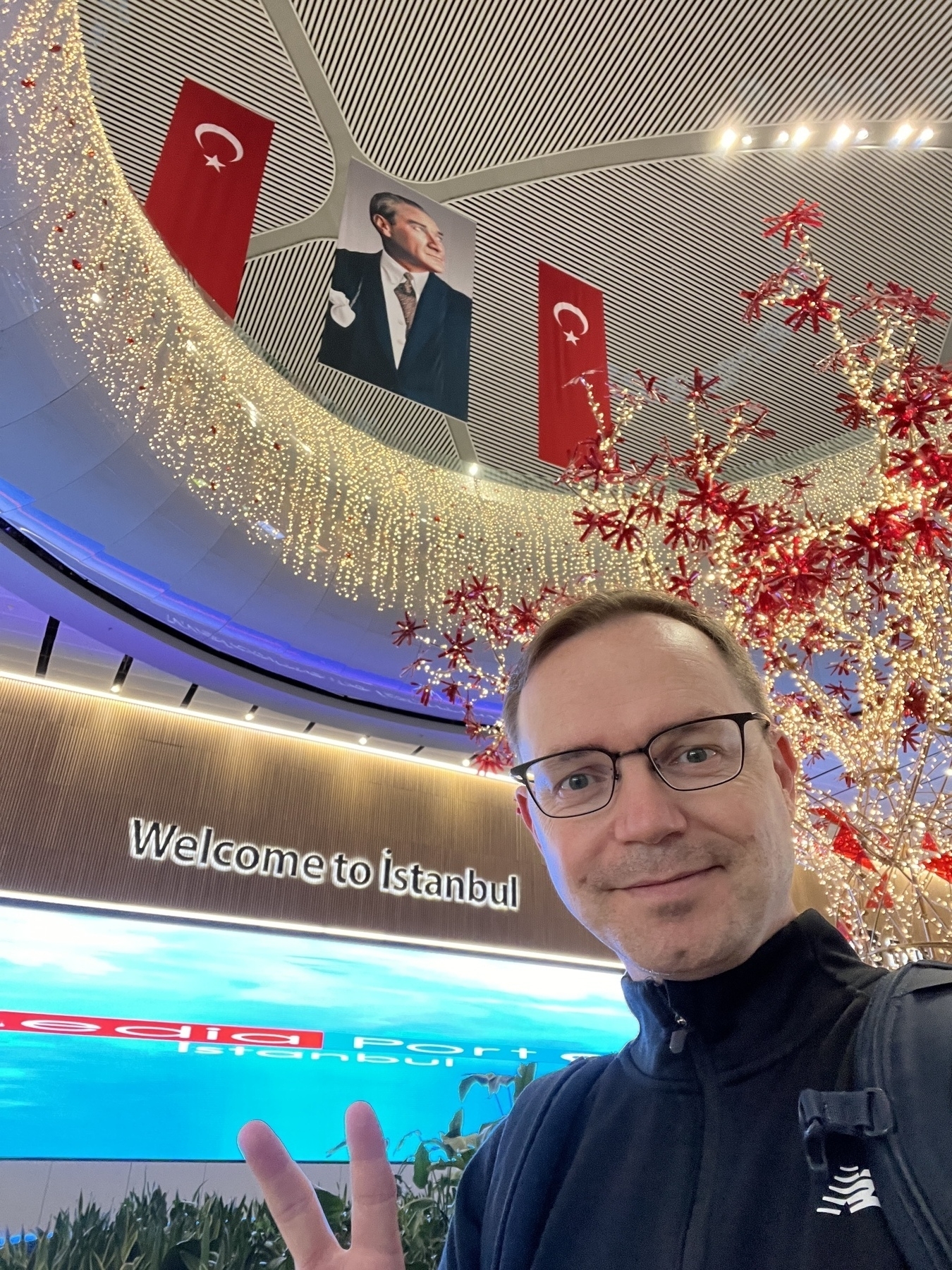 Chad selfie at the baggage claim exit in the Istanbul airport posing with the welcome sign, a huge light display, and a large image of Mustafa Kemal Attaturk
