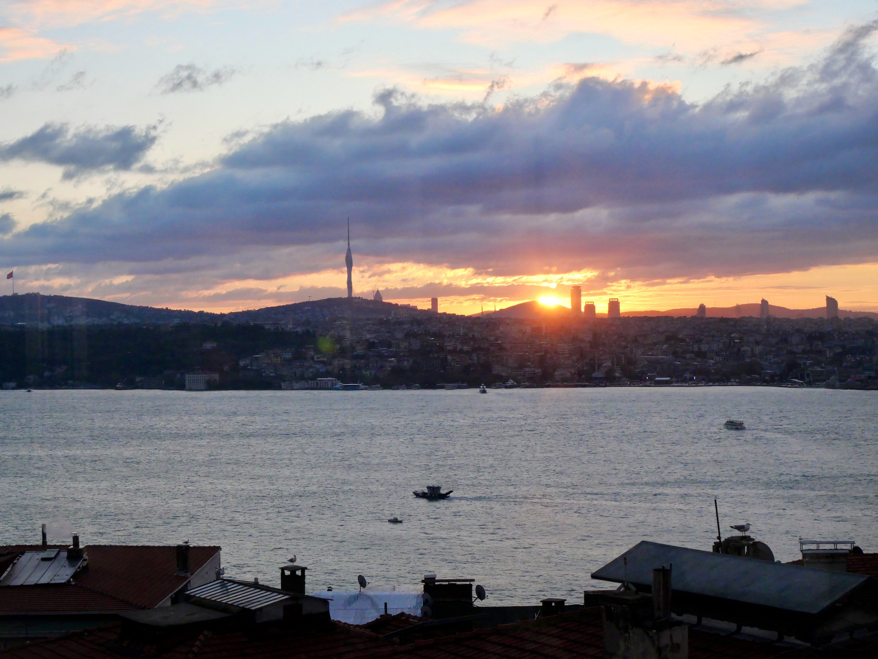 Sun rising over a mountain across a body of water. The silhouette of the Çamlıca Tower is clearly visible.