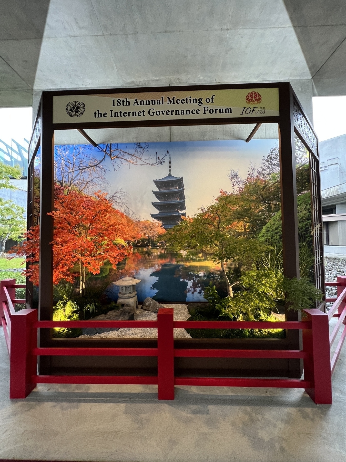 Entrance display featuring real maple trees arranged against a backdrop featuring a pagoda. Above is the sign “18th Annual Meeting of the Internet Governance Forum”