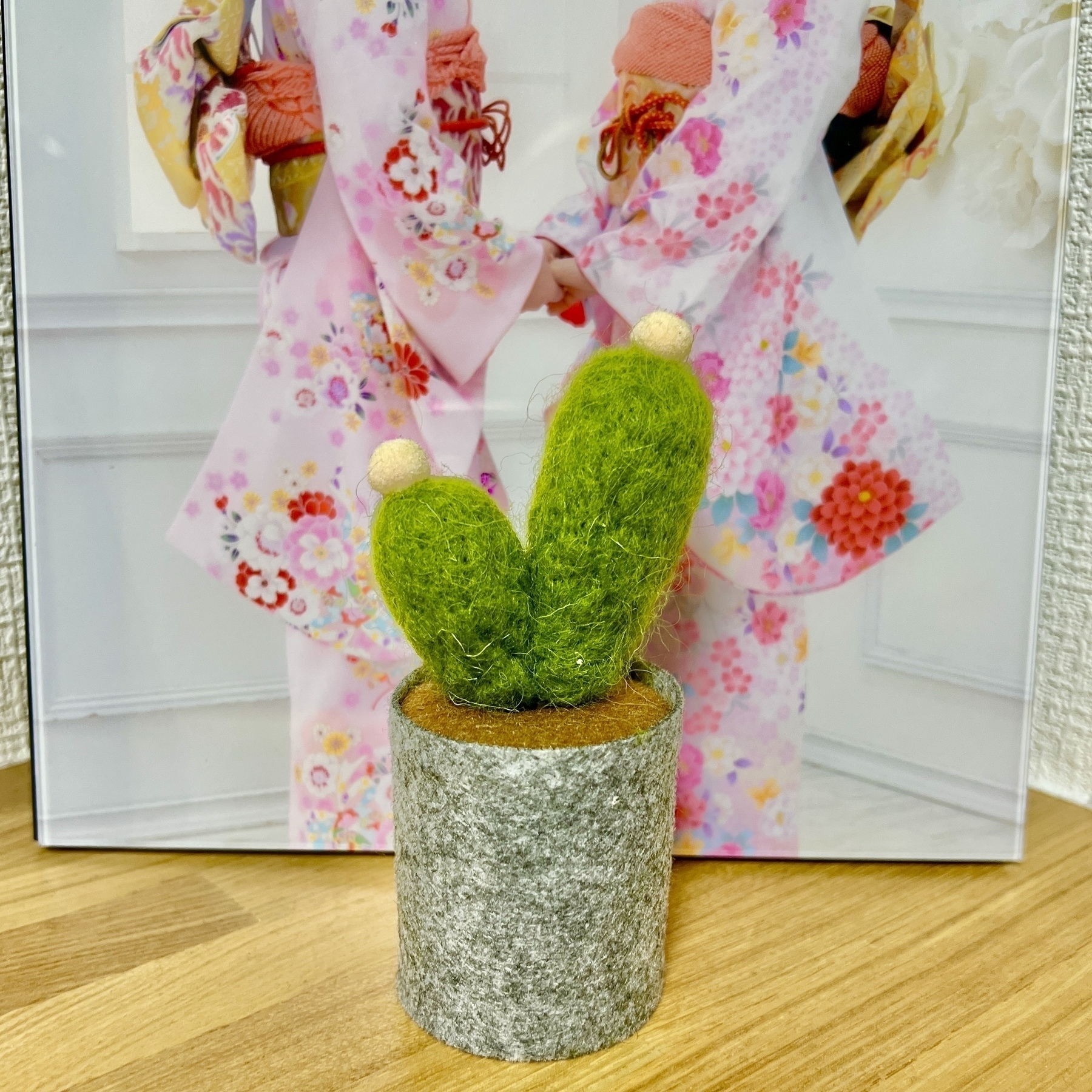A small felt cactus in front of a photo of two girls wearing bright kimono holding hands