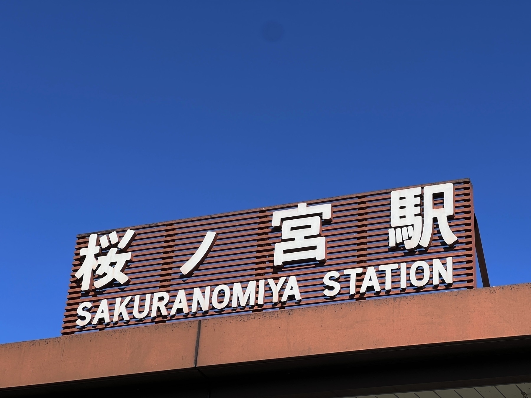 The sign for Sakuranomiya Station with deep blue  cloudless sky above