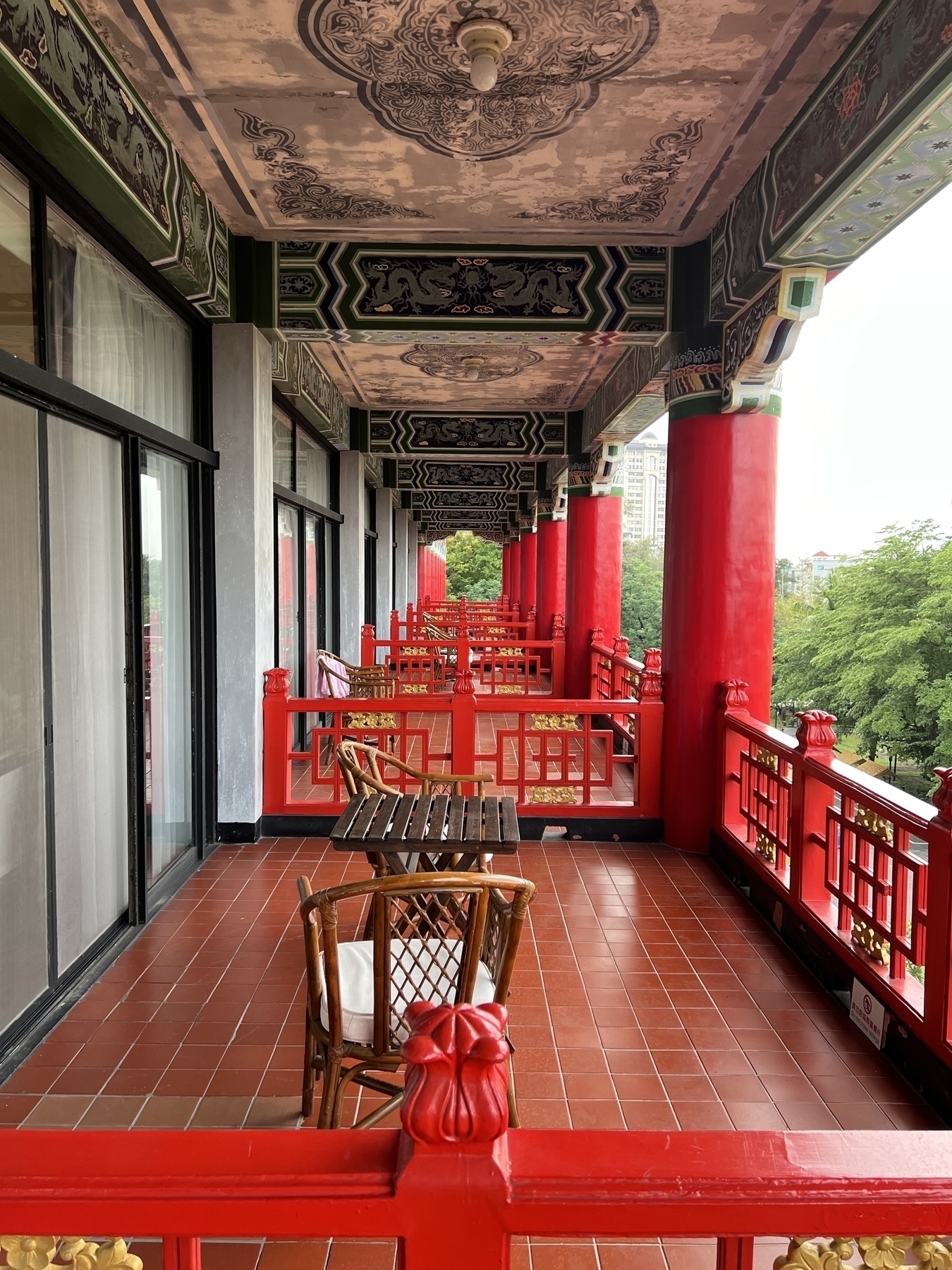 Photo along the balconies of the hotel. Each unit gets a large squarish tiled area with chairs and a table. Everything is painted in vermillion and symmetric