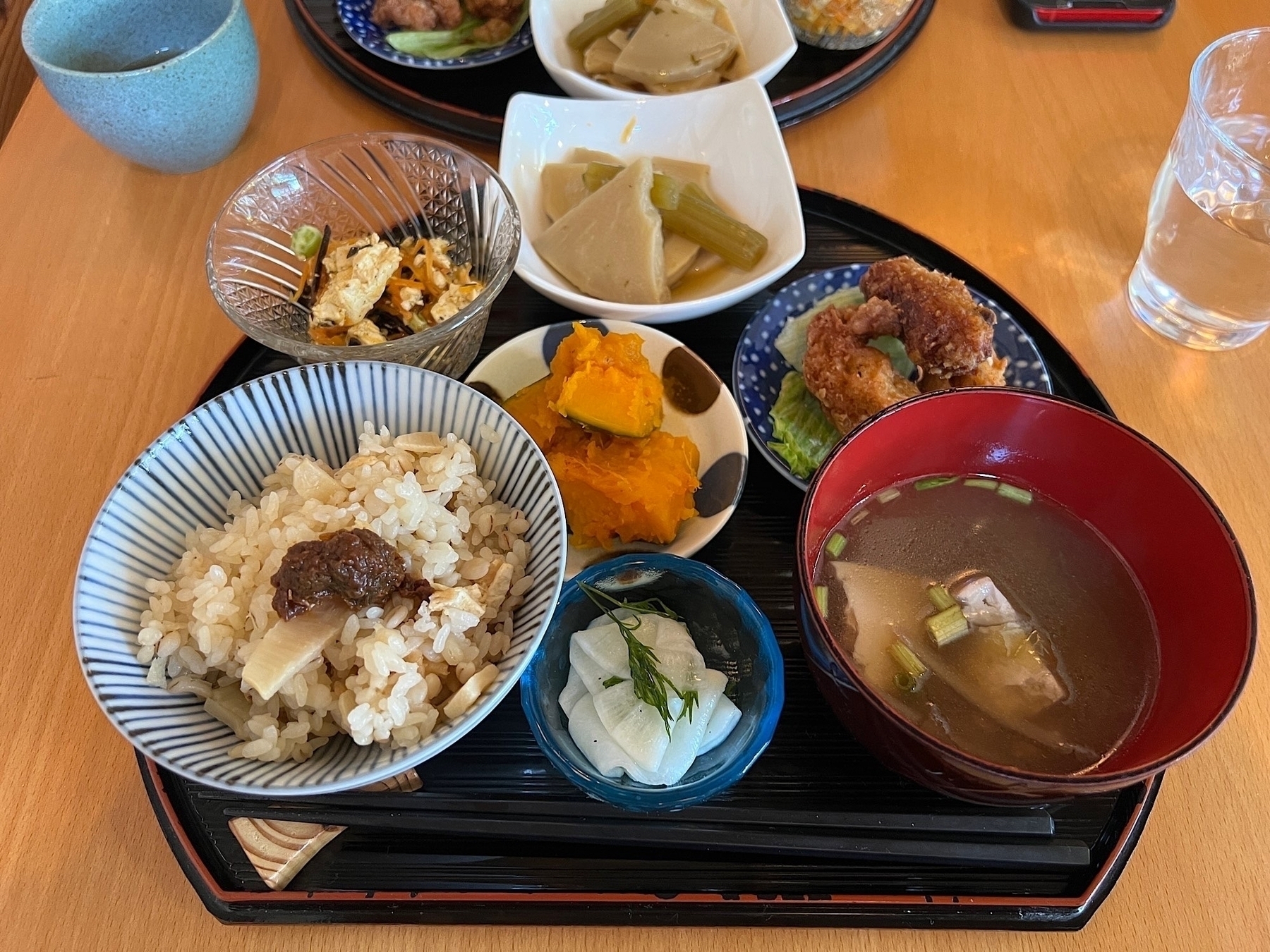 A tray with various dishes including bamboo shoots rice, miso soup, something that looks like fried chicken but is tofu, pickled daikon, pumpkin, etc