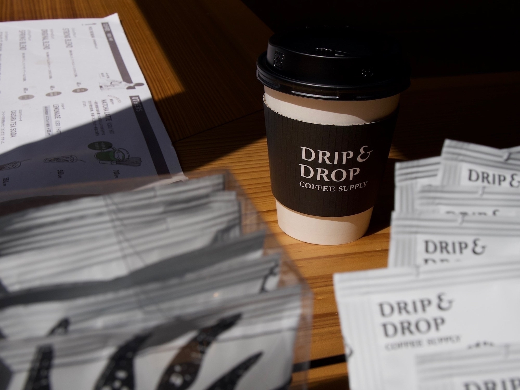 A Drip & Drop branded paper coffee cup sitting in the sunlight