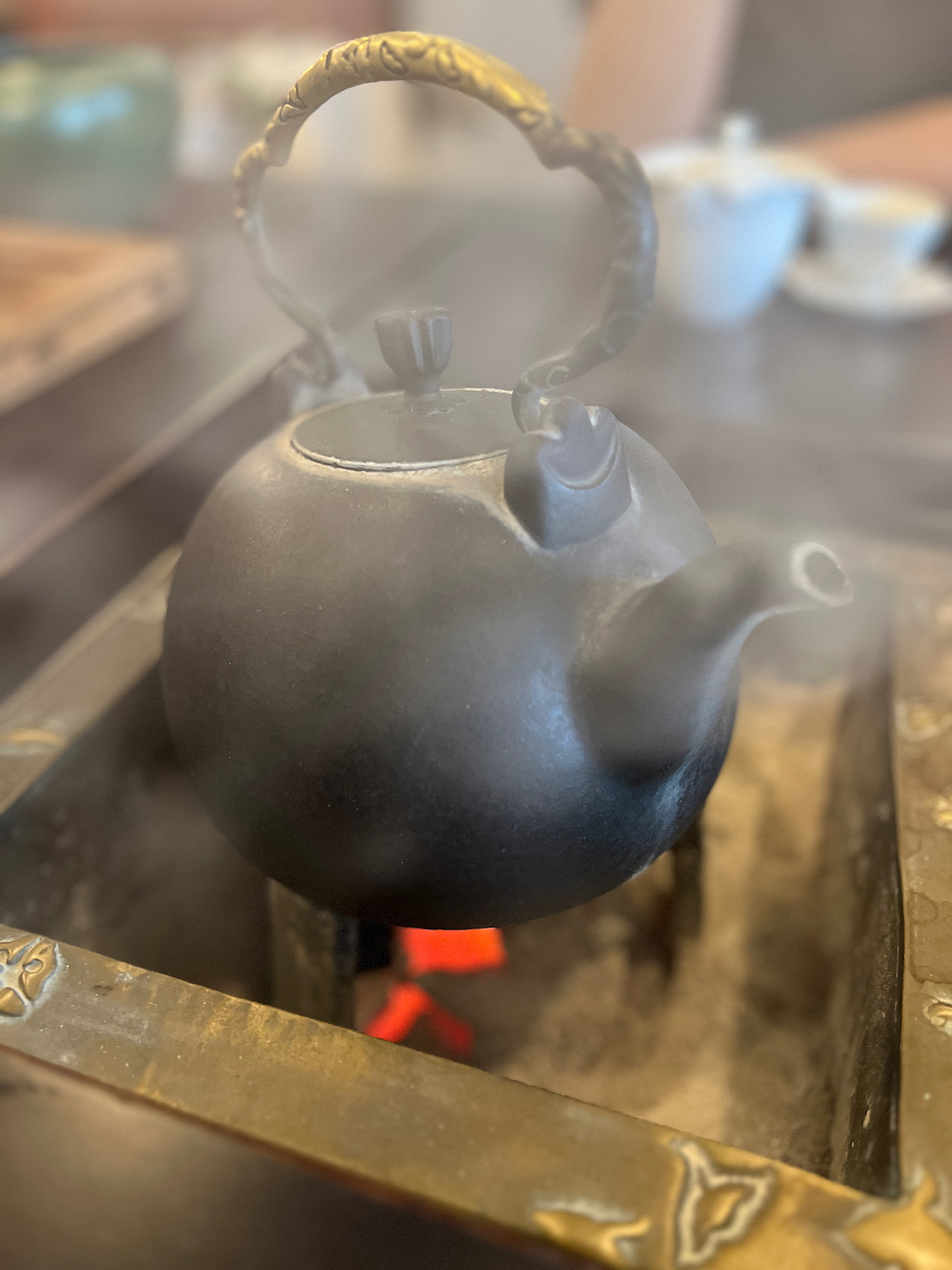 An iron tea pot over coals steams warmly