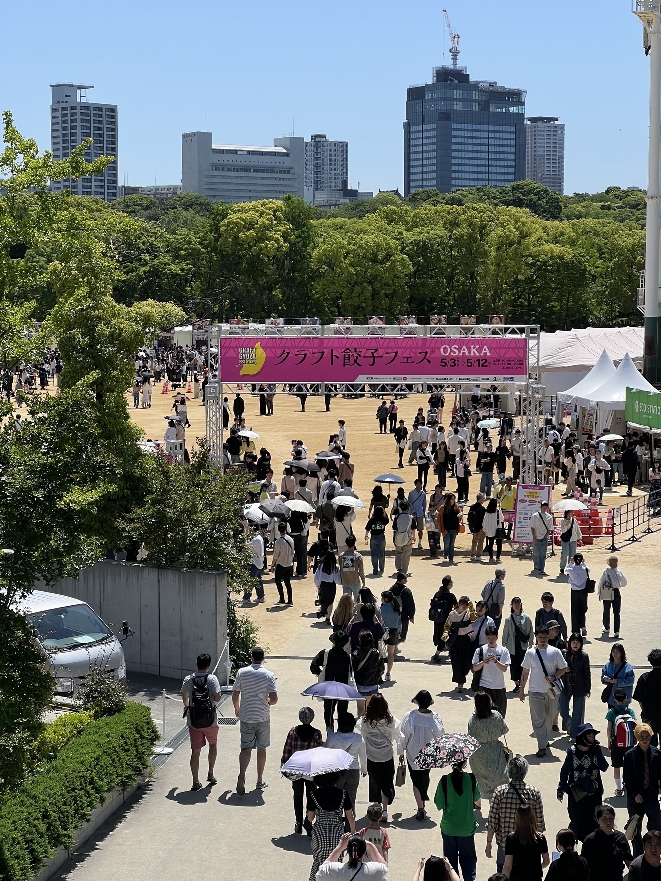 Long shot of people walking under a pink banner advertising the Craft Gyoza Fest 2024 on a bright sunny day