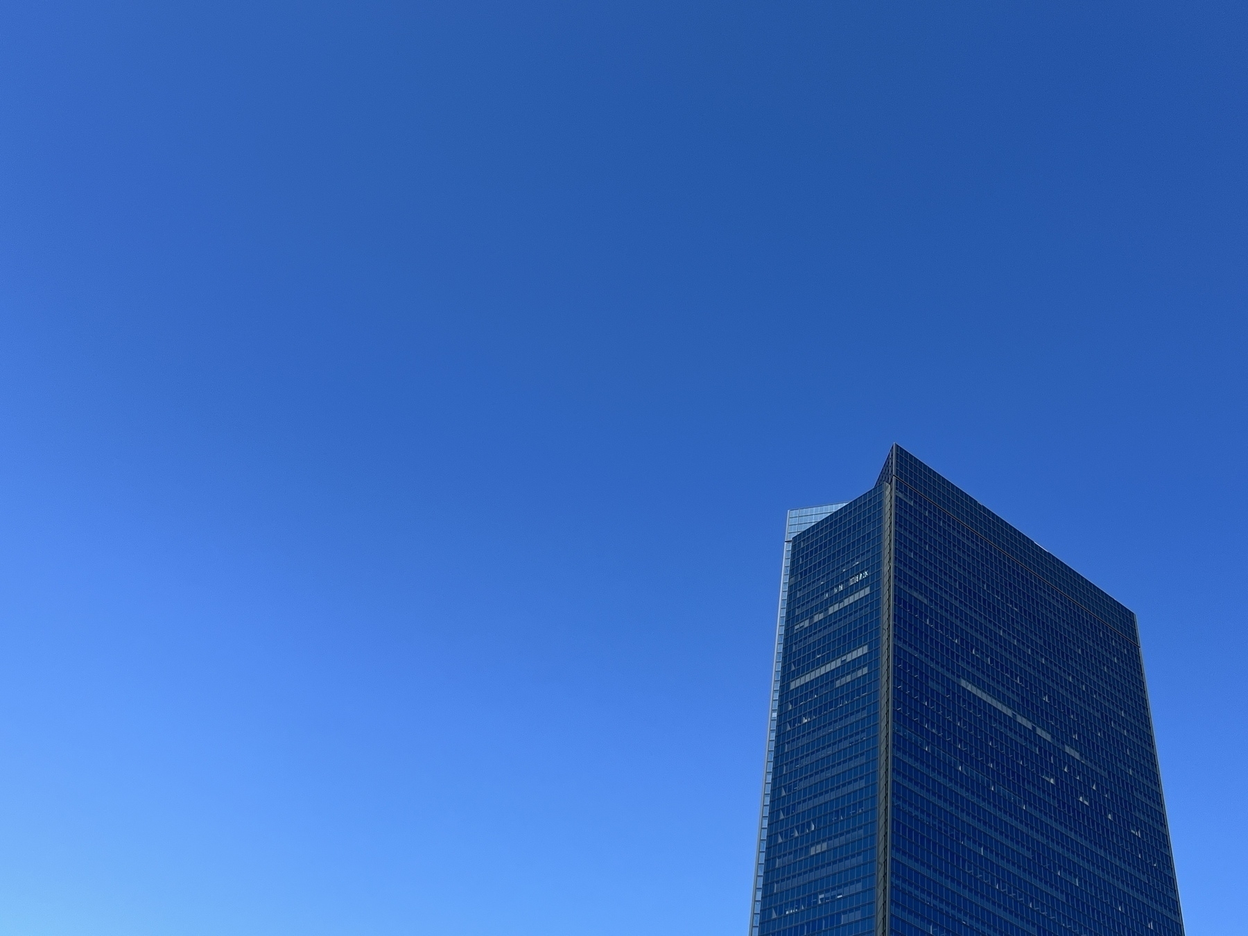 Photo of a cloudless blue sky. To the bottom right is a building with a dark glass blue colour