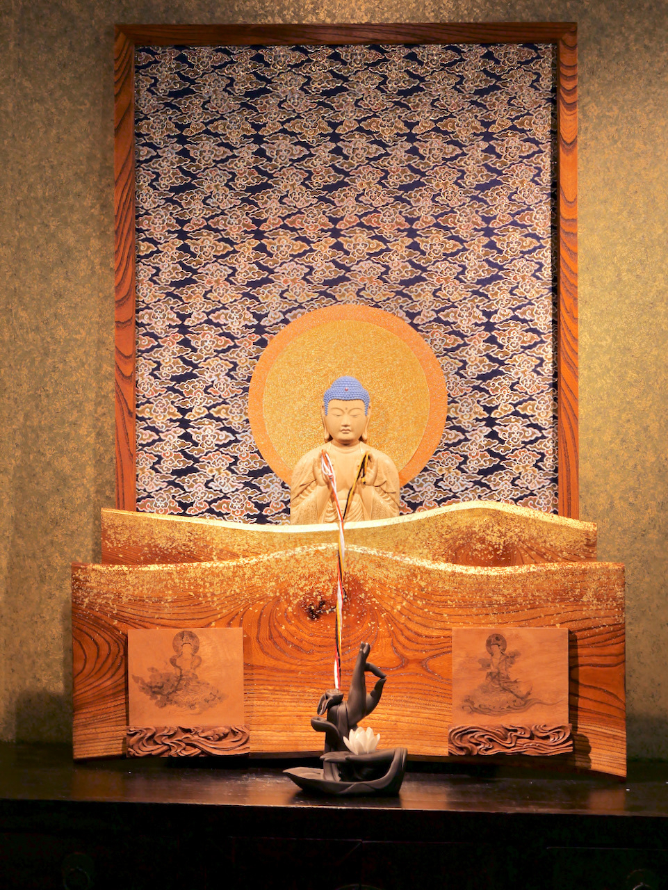 a wooden Amida relief against a cloud pattern cloth. The Amida is holding two strings that hang down over a third part of the artwork showing Kannon and Seishi-bosatsu