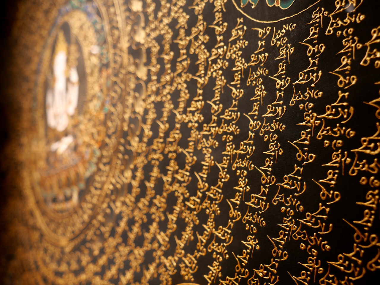 Closeup of Tibetan writing in gold ink that rises from the black paper
