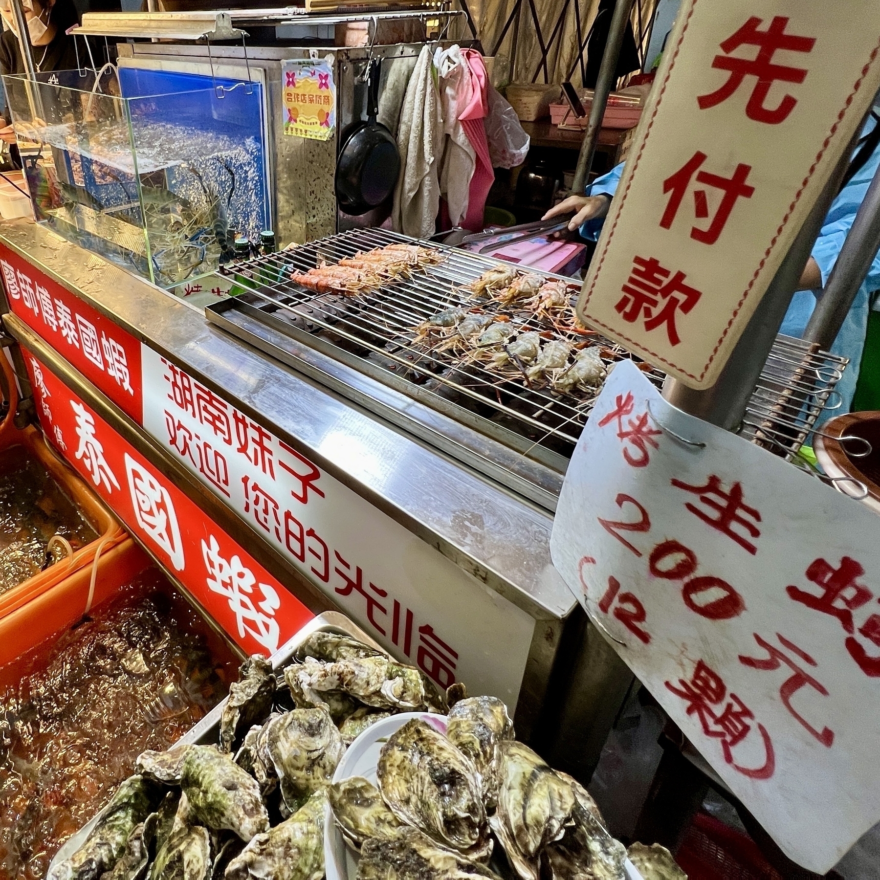 A roasted giant shrimp stand. A pile of clams are out front of the shop stall