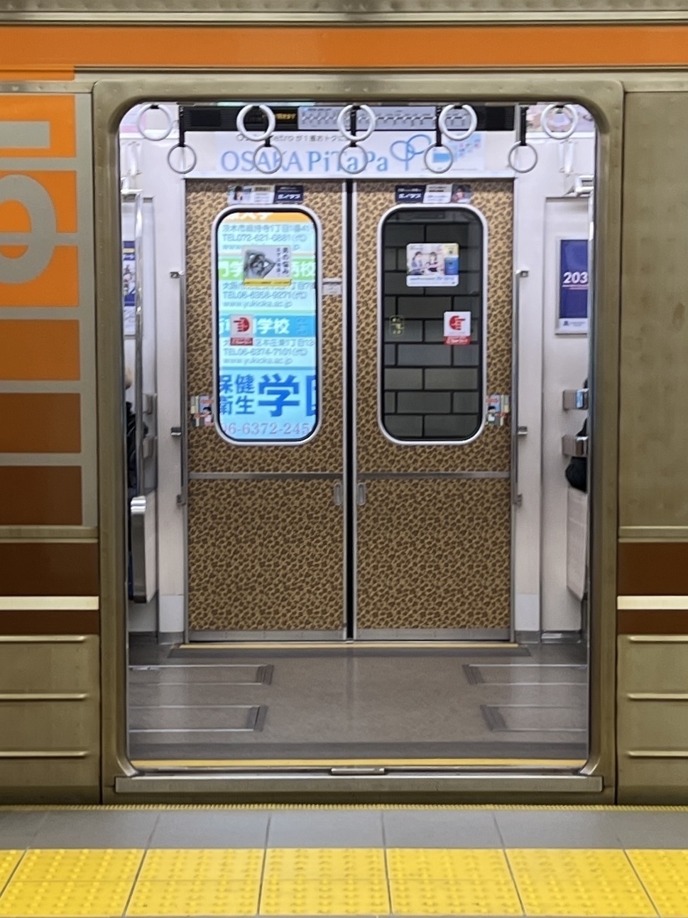 Osaka Metro subway car doors open revealing the interior. The doors on the other side have a leopard print design