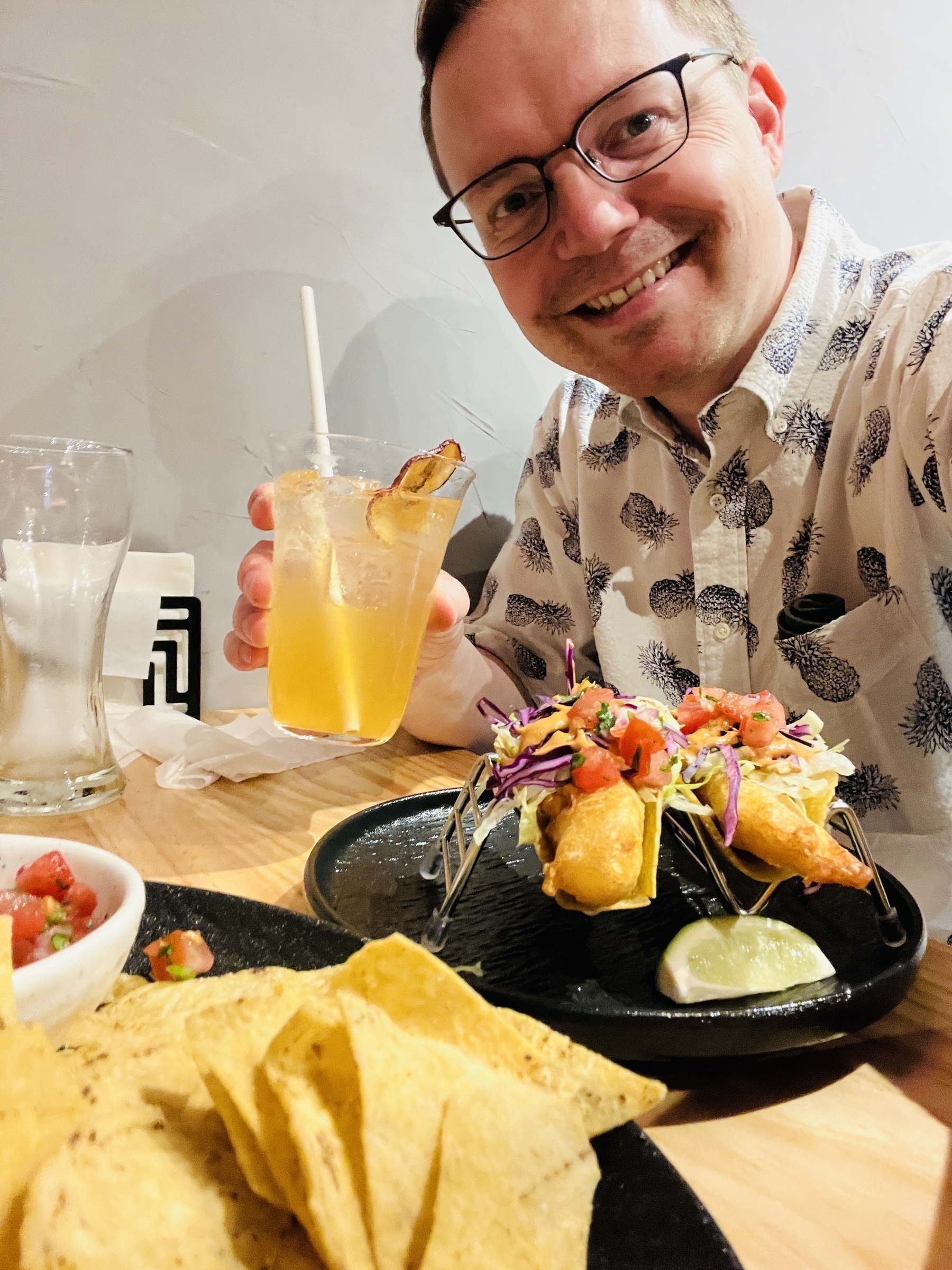 Chad hovering menacingly over some fish tacos and a plate of chips and salsa, holding a fruity tea beverage