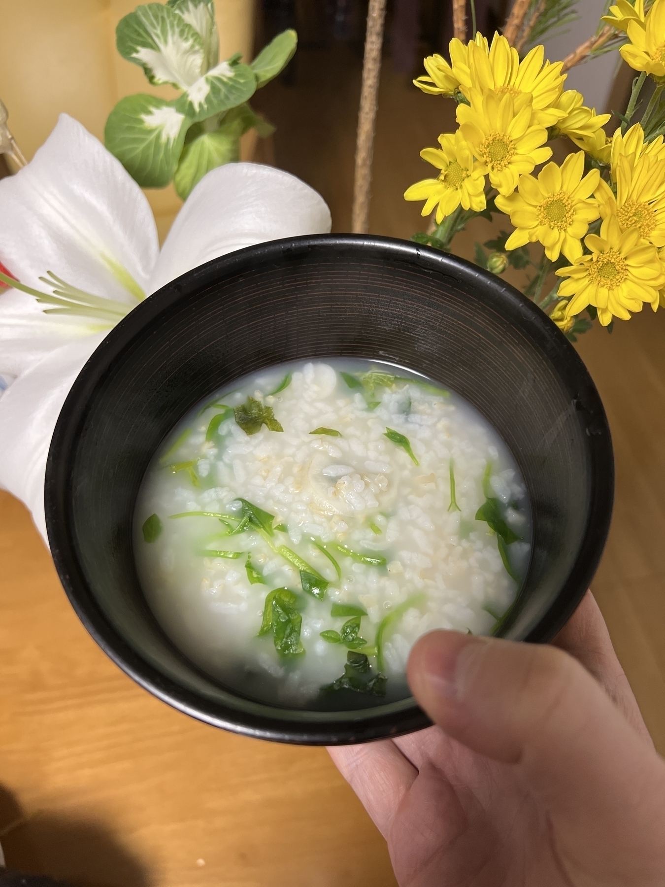 A bowl of rice porridge with a number of visible green herbs