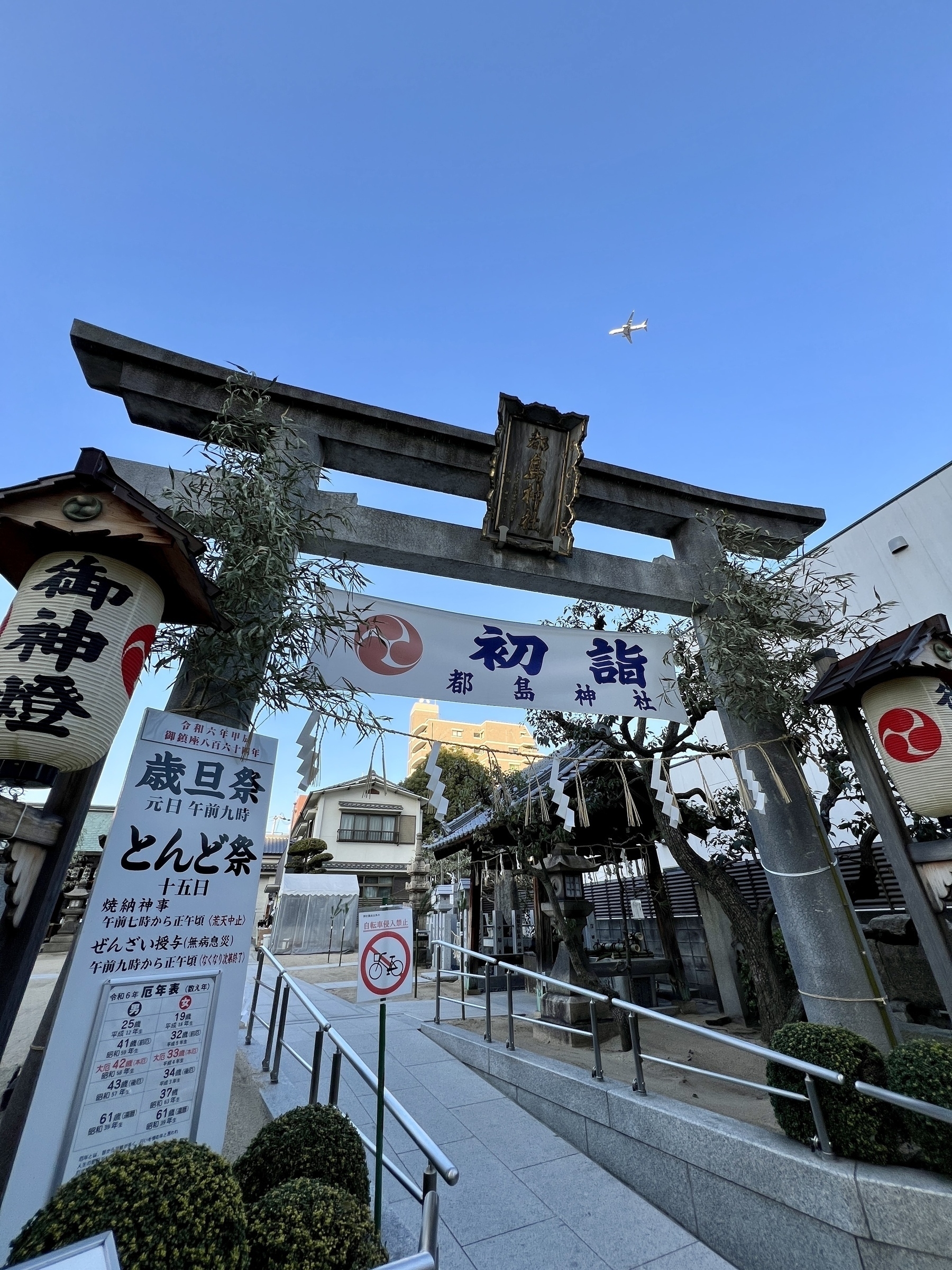 Stone Torii at a shrine with new years decorations. Airplane flies over in the blue sky above