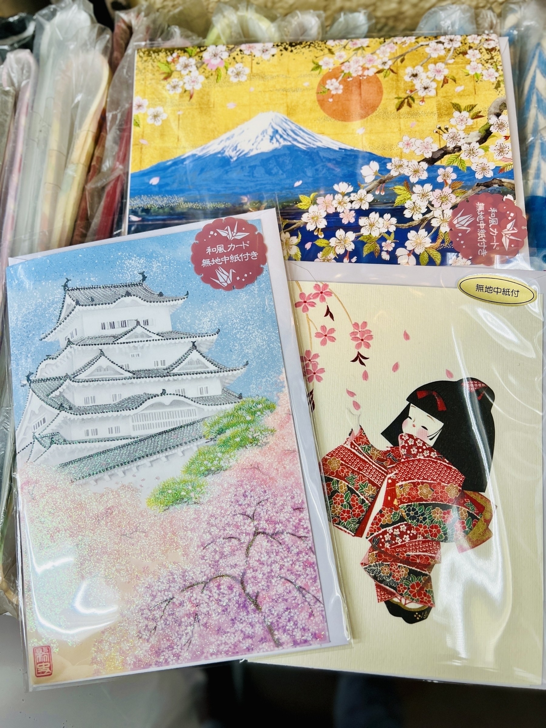 3 greeting cards: One depicts Mt Fuji with cherry blossom trees in the foreground. Another is cherry blossoms with Himeji Castle in the background. The third is a kokeshi like doll-girl reaching up to catch falling sakura petals