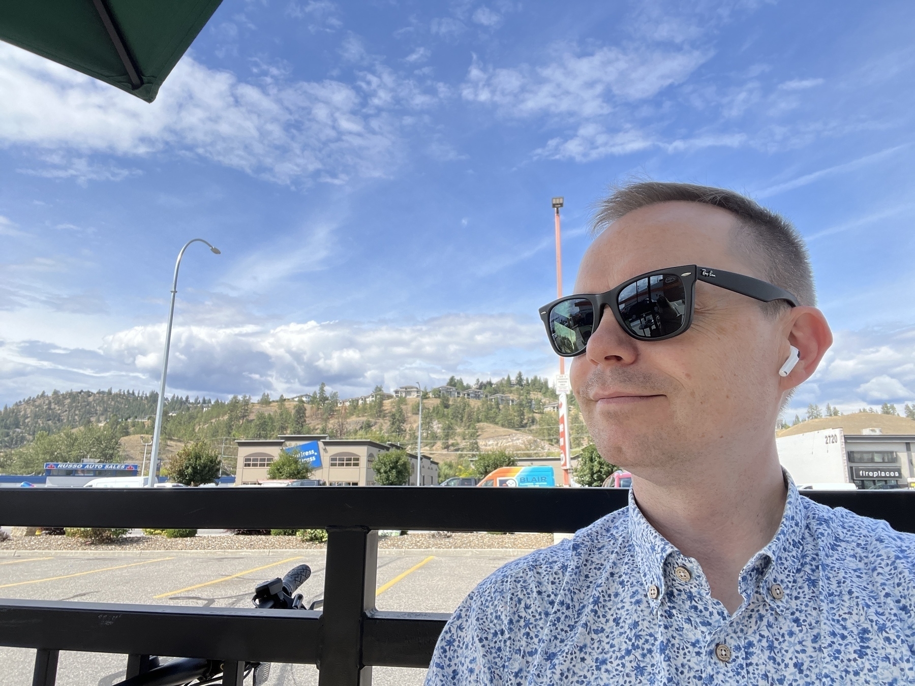 Chad selfie on a patio wearing sunglasses. Bright blue sky and dry hills of Kelowna in the background