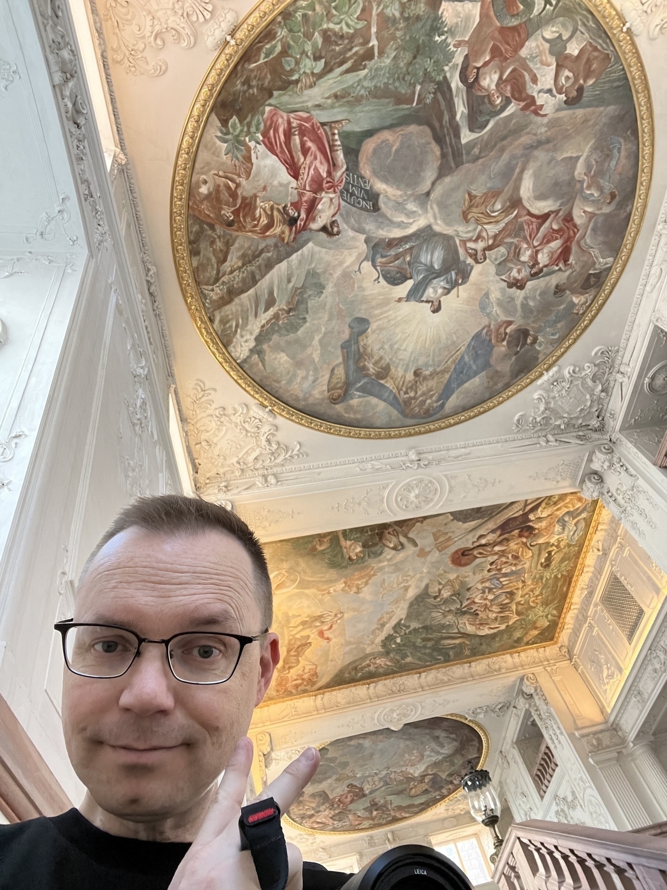 Low angle Chad selfie flipping the reverse peace sign, the ceilings above adorned with baroque early 18th C paintings of angels and civilizing Roman figures