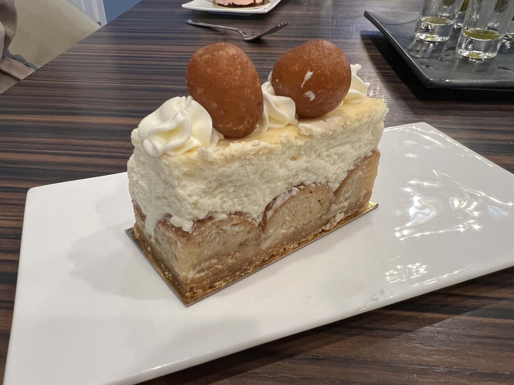 A slice of cheese cake with two small gulabjamun balls on top. The base of the cake is made from large quartered gulabjamun