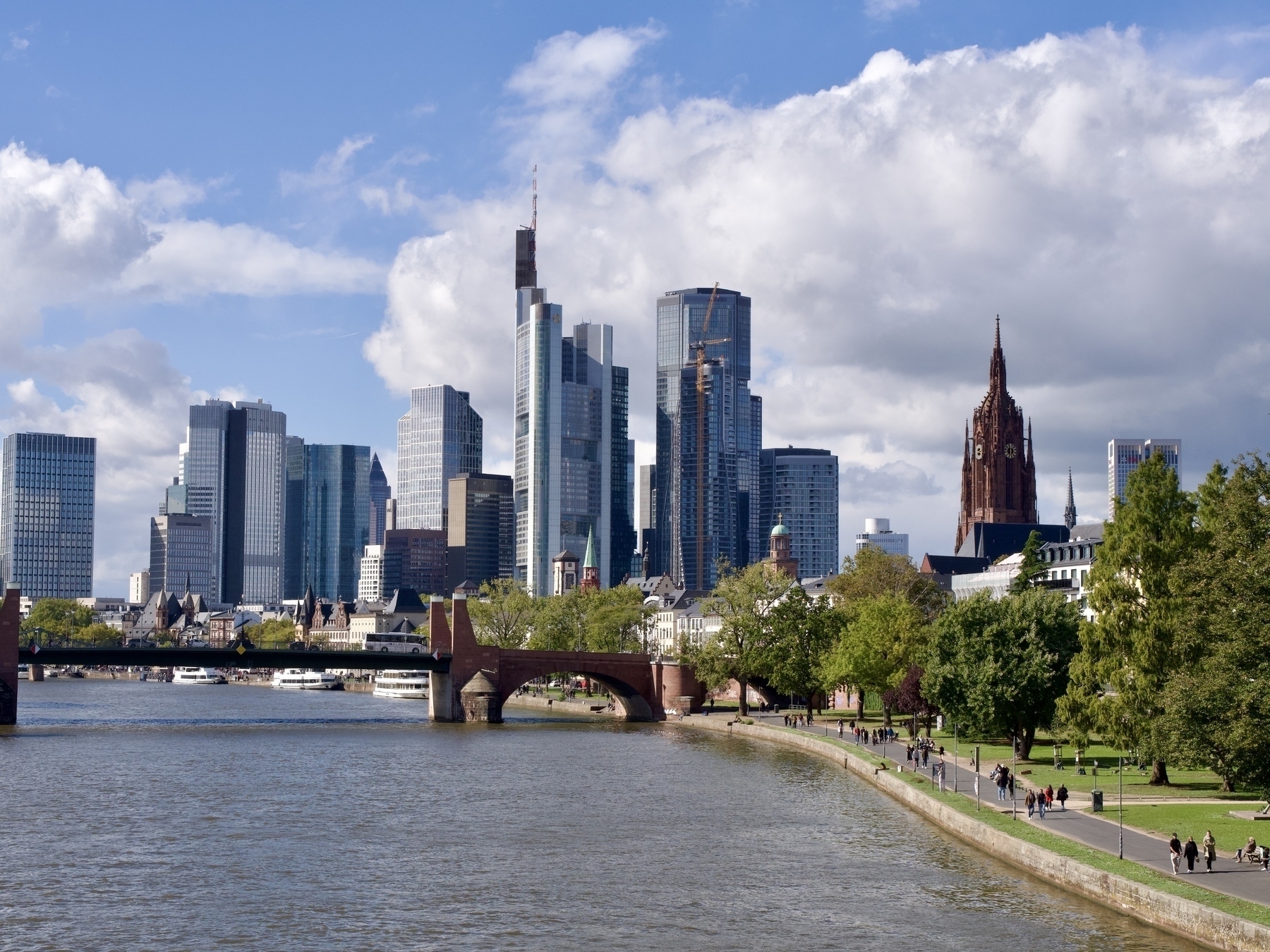 A river in the foreground. Tall buildings of a city in the distance. To the right is an old cathedral bell tower 