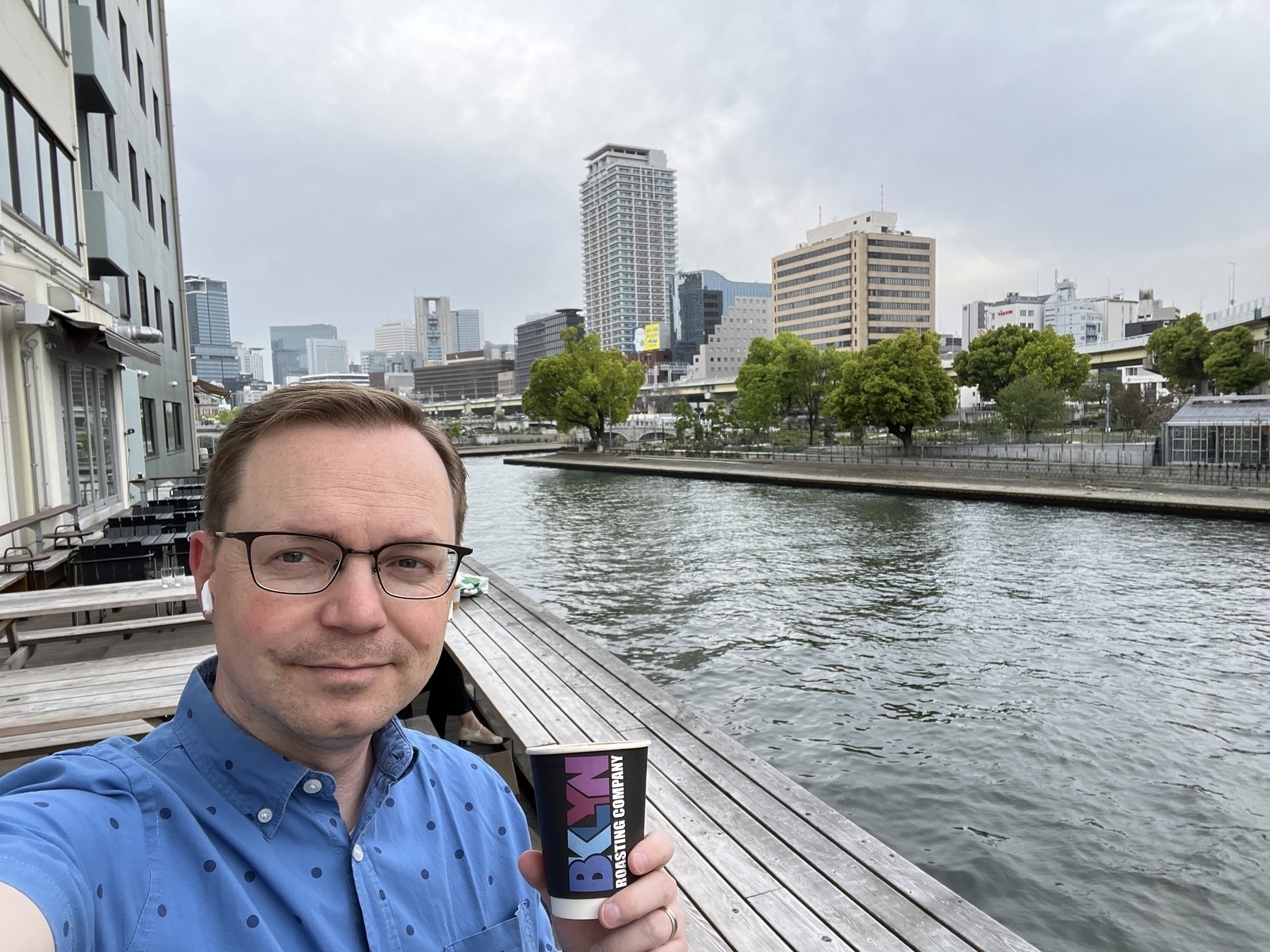 Chad stands on a riverside patio holding a Brooklyn Roasters coffee cup