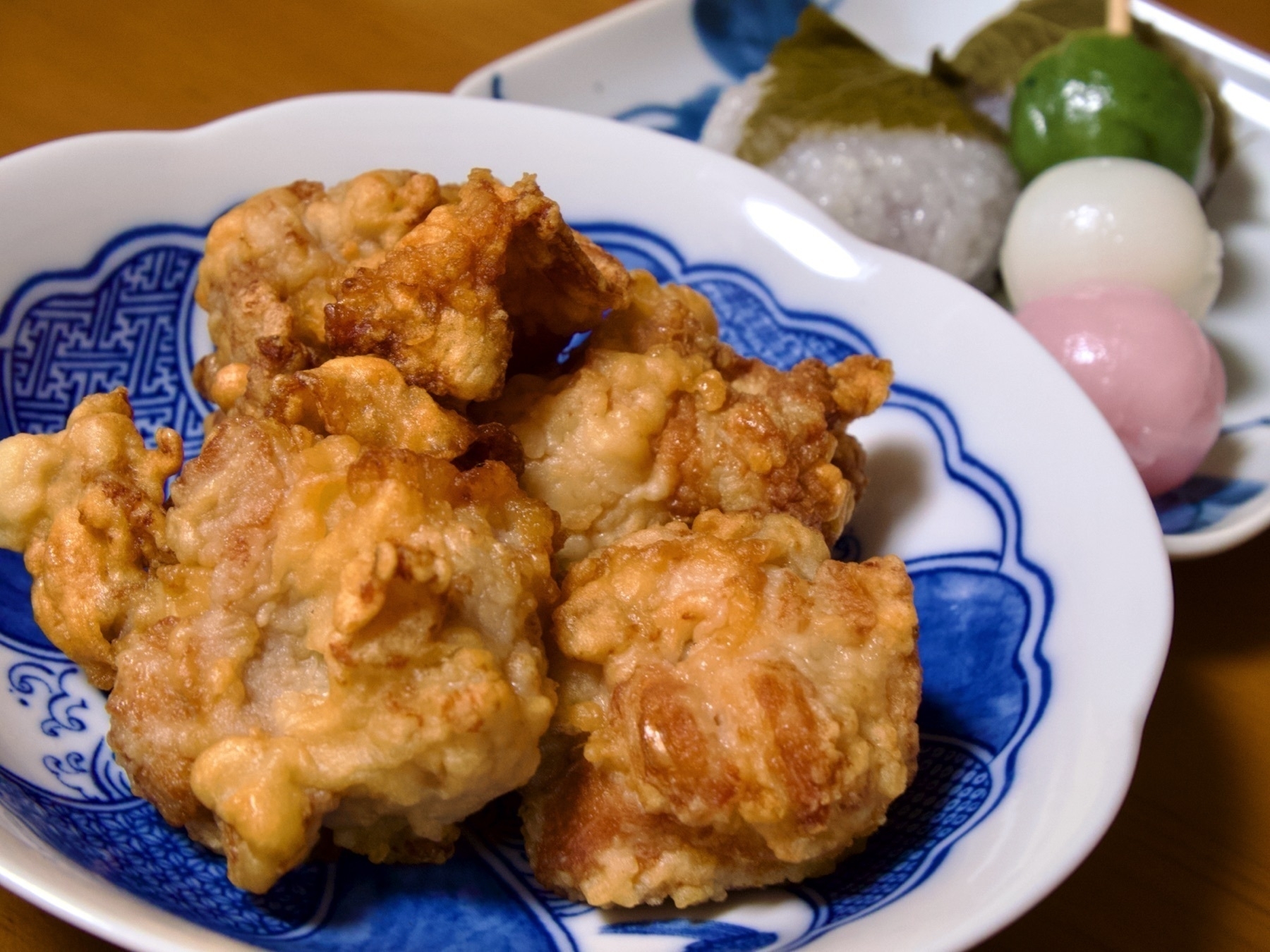 a plate of karaage and a plate with two pieces of sakura-mochi and a stick of three coloured hanami dango