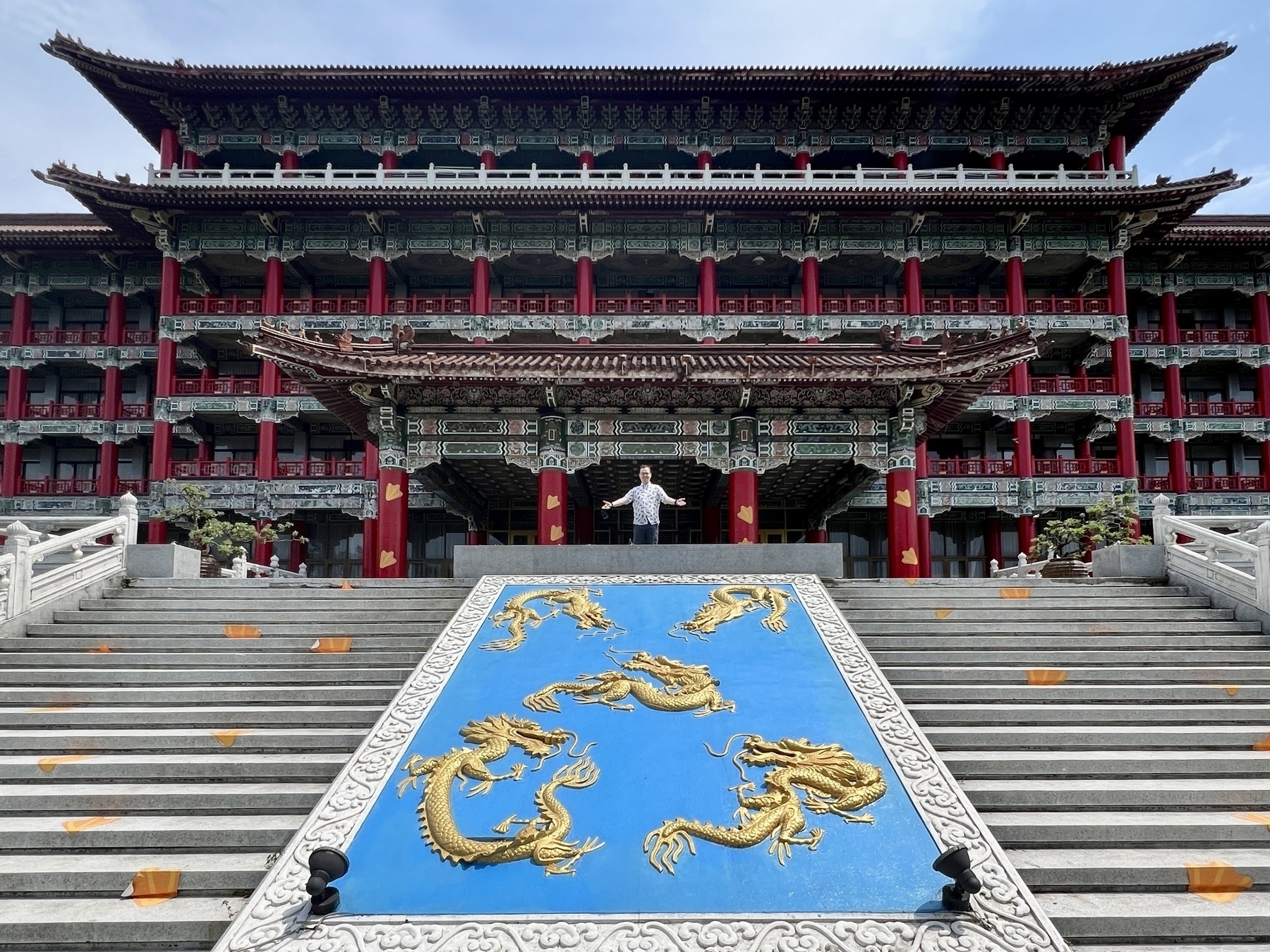 Chad stands at the entrance to the hotel, atop a staircase decorated with golden dragons, arms outstretched in a welcoming motion