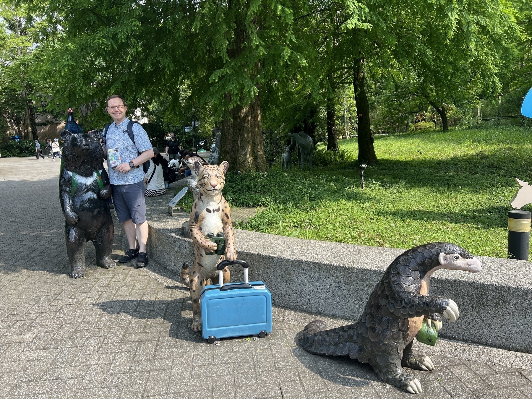 Chad poses with statues of animals like a sun bear, leopard, and pangolin at the zoo entrance