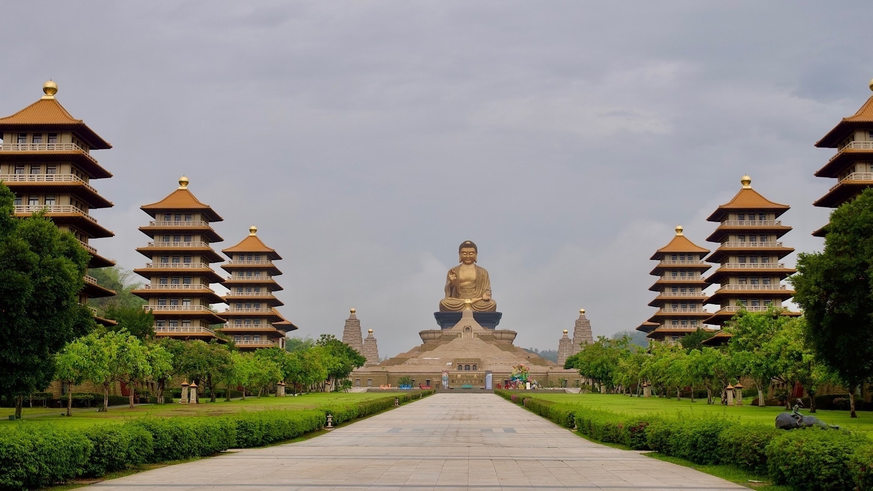 a wide boulevard lined with trees and pagodas leading to a huge Buddha statue