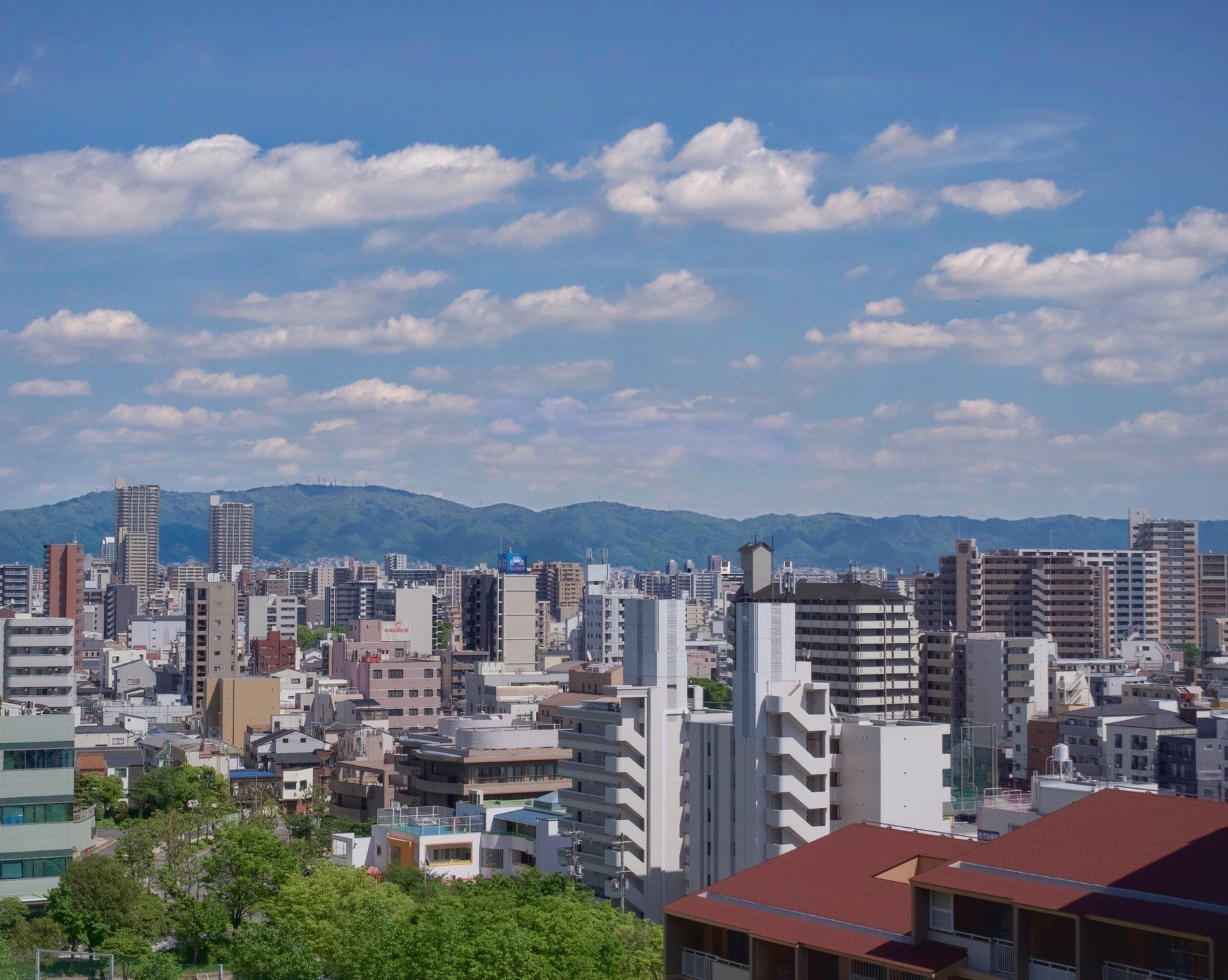 Landscape photo on a sunny day with clouds of buildings receding into the distance and a mountain range beyond