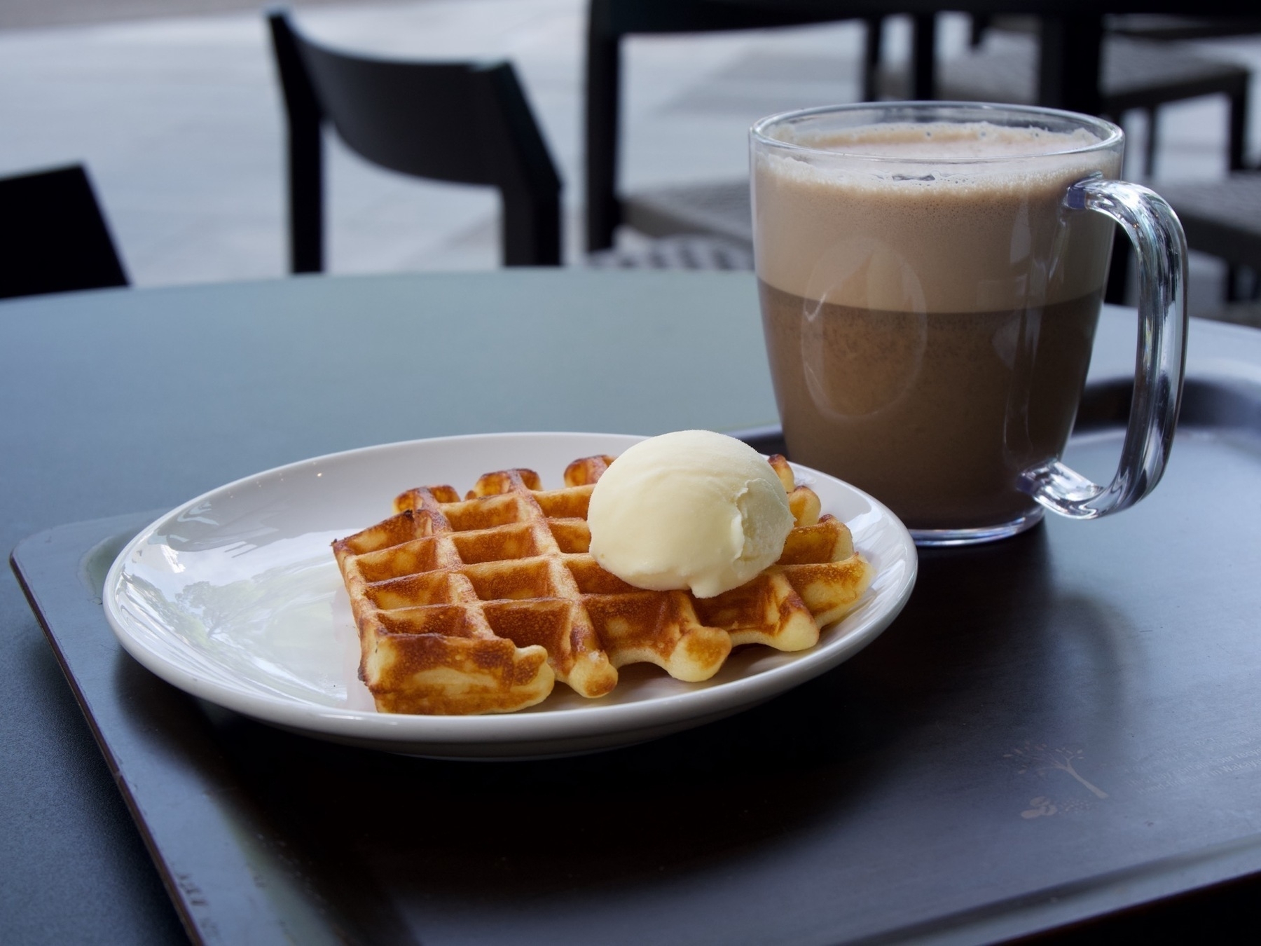 A glass mug of tea latte and a plate with a waffle. On top of the waffle is a scoop of ice cream