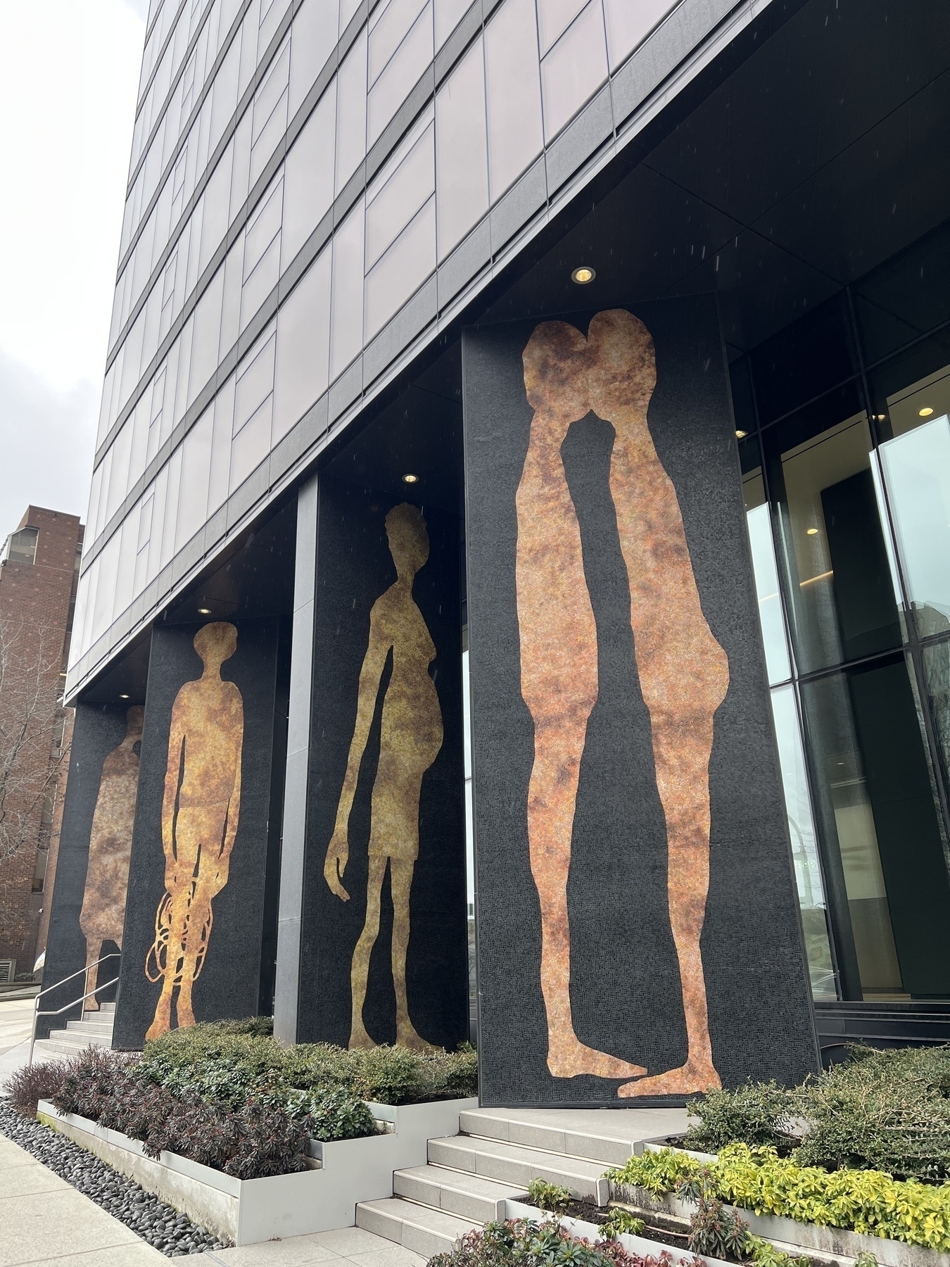 Pillars at the entrance of a building with large silhouettes of people in different poses. Hard to explain what I am seeing here. One pillar shows two people kissing. Another of a figure with elongated arms. 