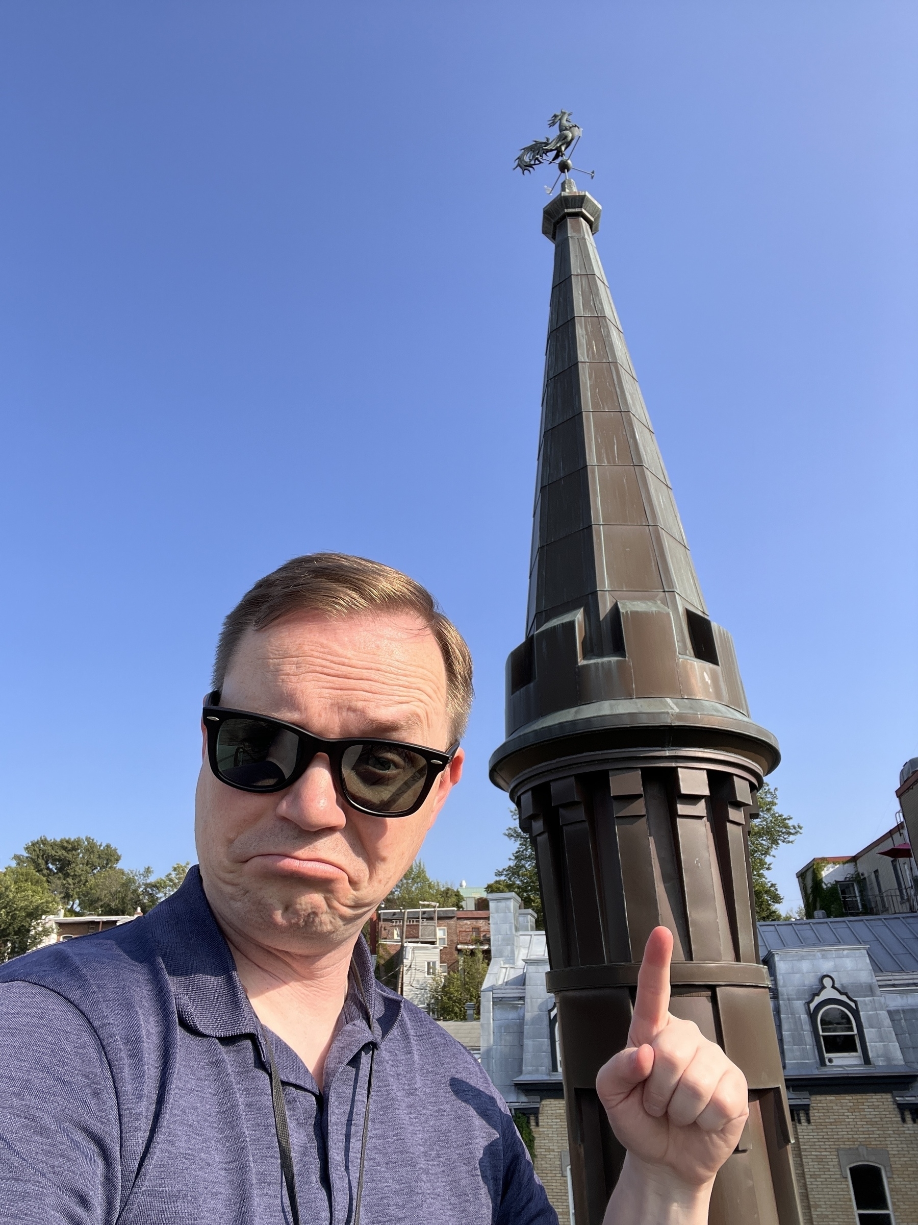 Chad selfie in front of a conicle turret topped with a weathervane. He is making some sort of “isn’t this fancy” stank face expression with one raised eyebrow