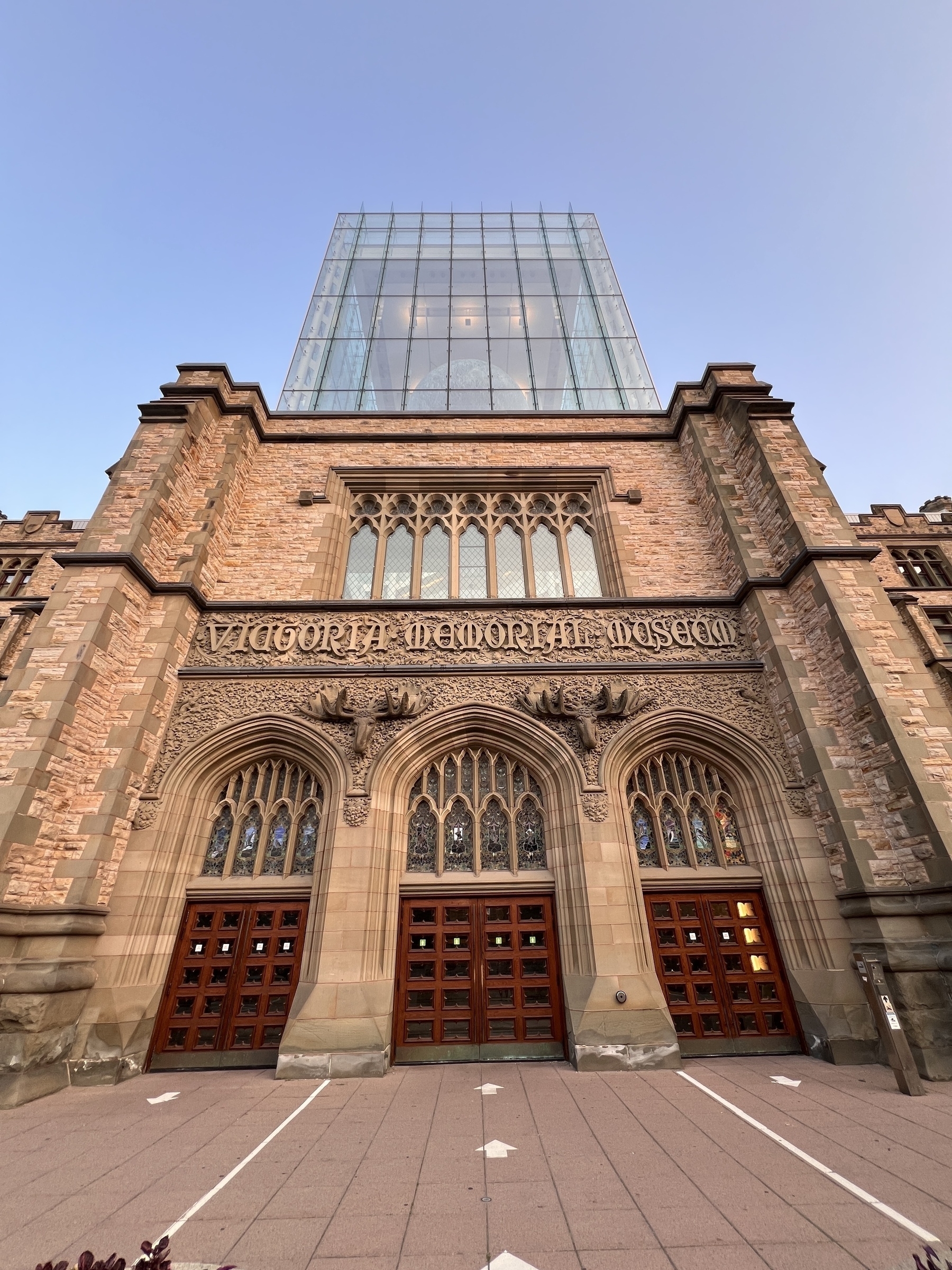 Front of a stone building with stone moose heads above the doors. The third floor is a giant glass cube with a Moon inside