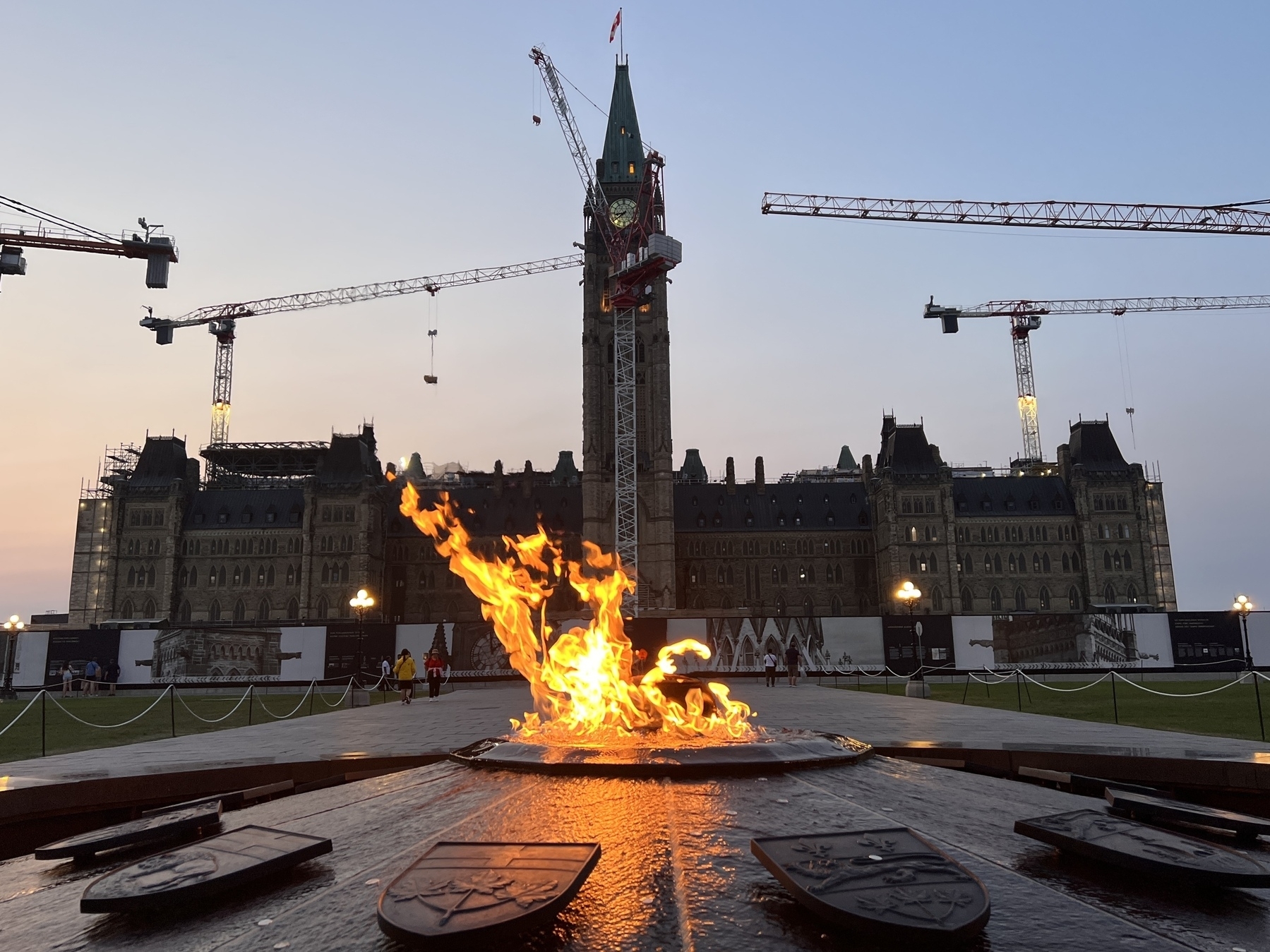 Canada Parliament Building at dusk. There are many tower cranes as the place is under renovation. In the foreground is the Flame of Confederation 