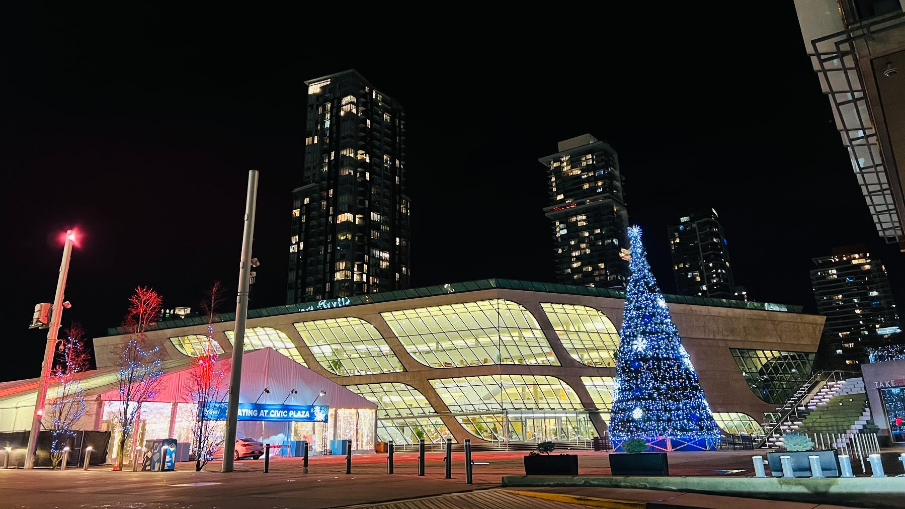 Wide angle shot of a rhomboid building. In from is a super tall Xmas tree all lit up.