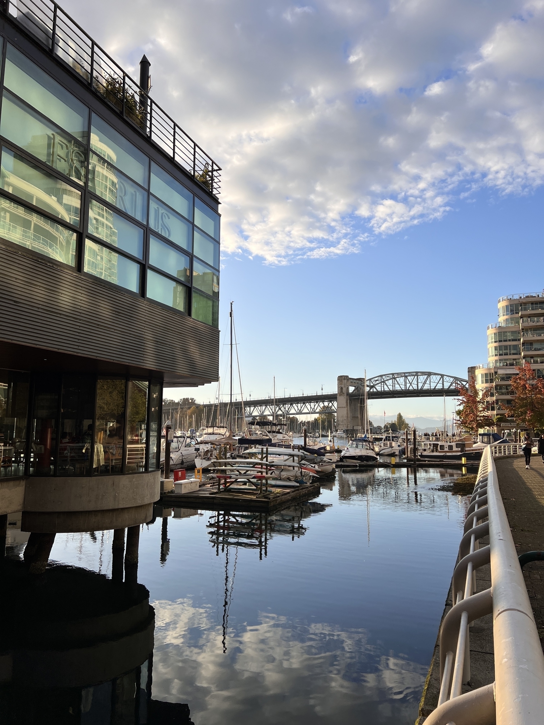 False Creek Yacht club building from water level. In the background is the marina and Burrard Bridge. The sky reflects in the calm water. 