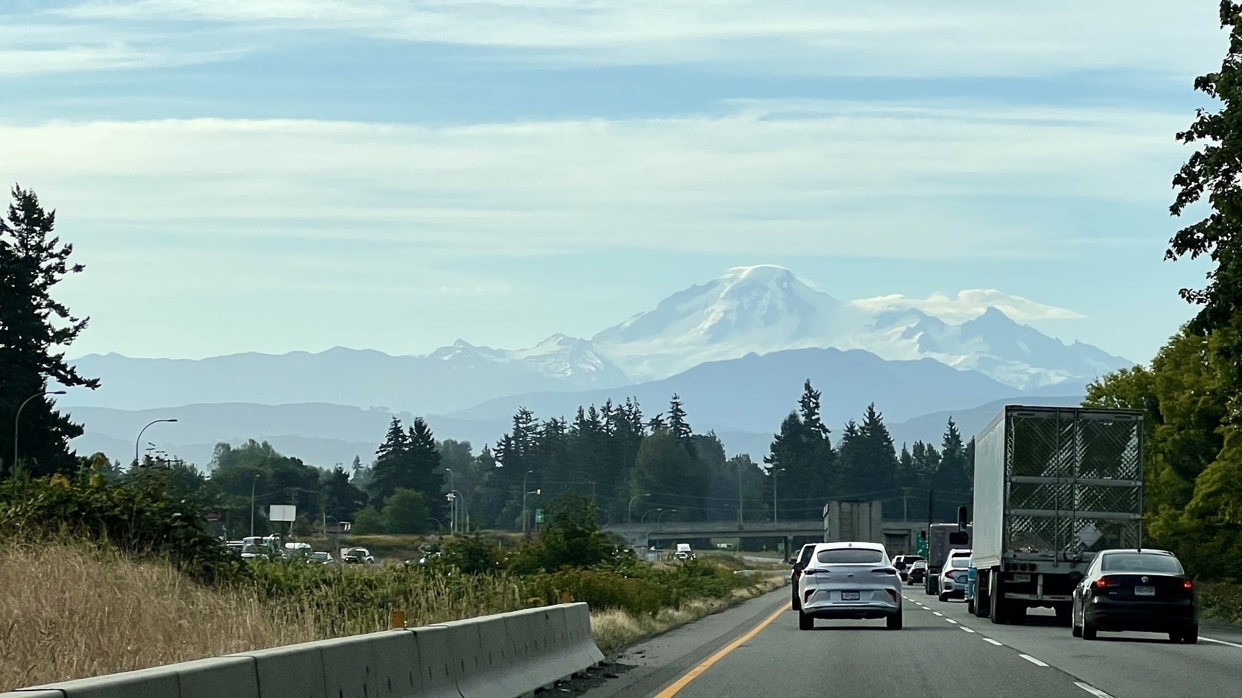 Photo from a highway with lots of traffic heading towards a tall snowy mountain in the distance 