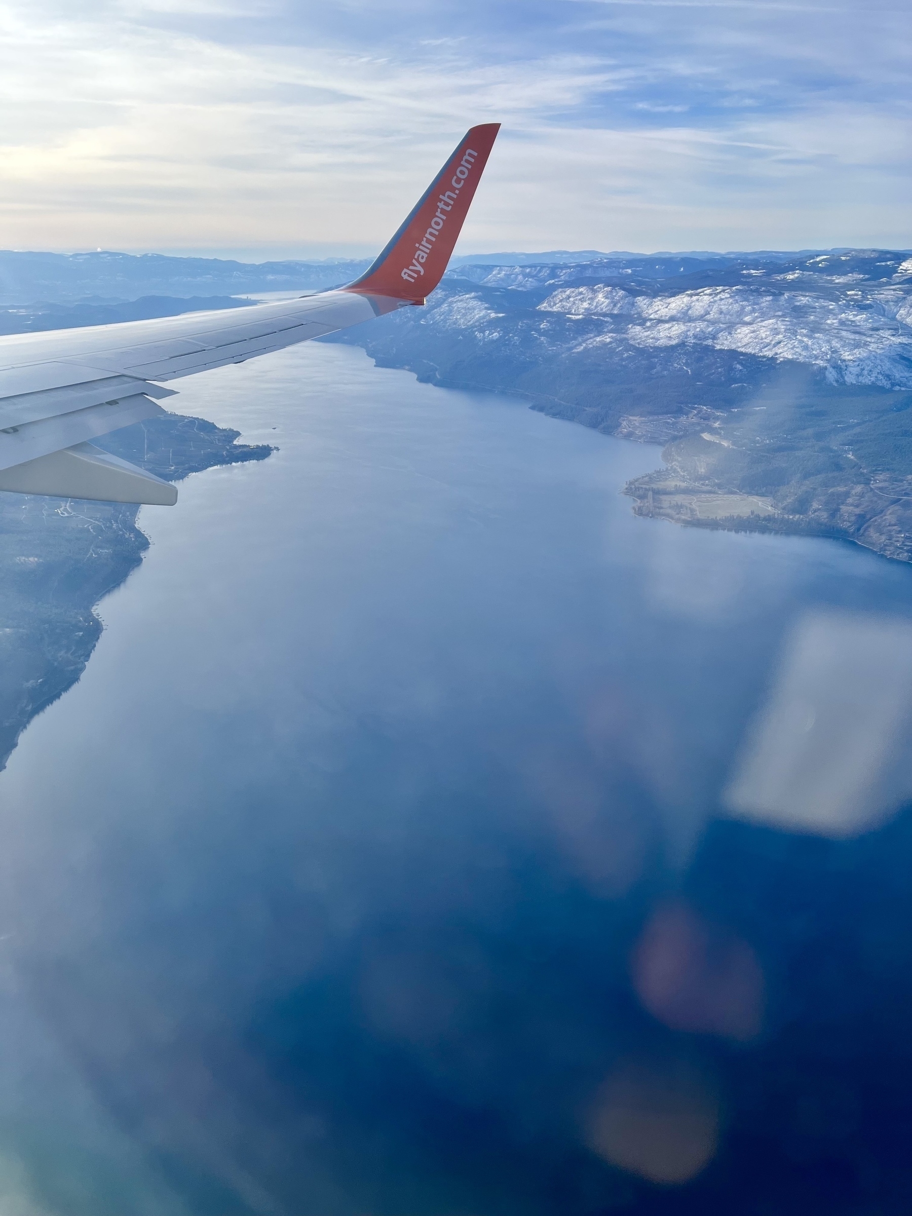 Photo from airplane window showing airplane wing and a large lake below 