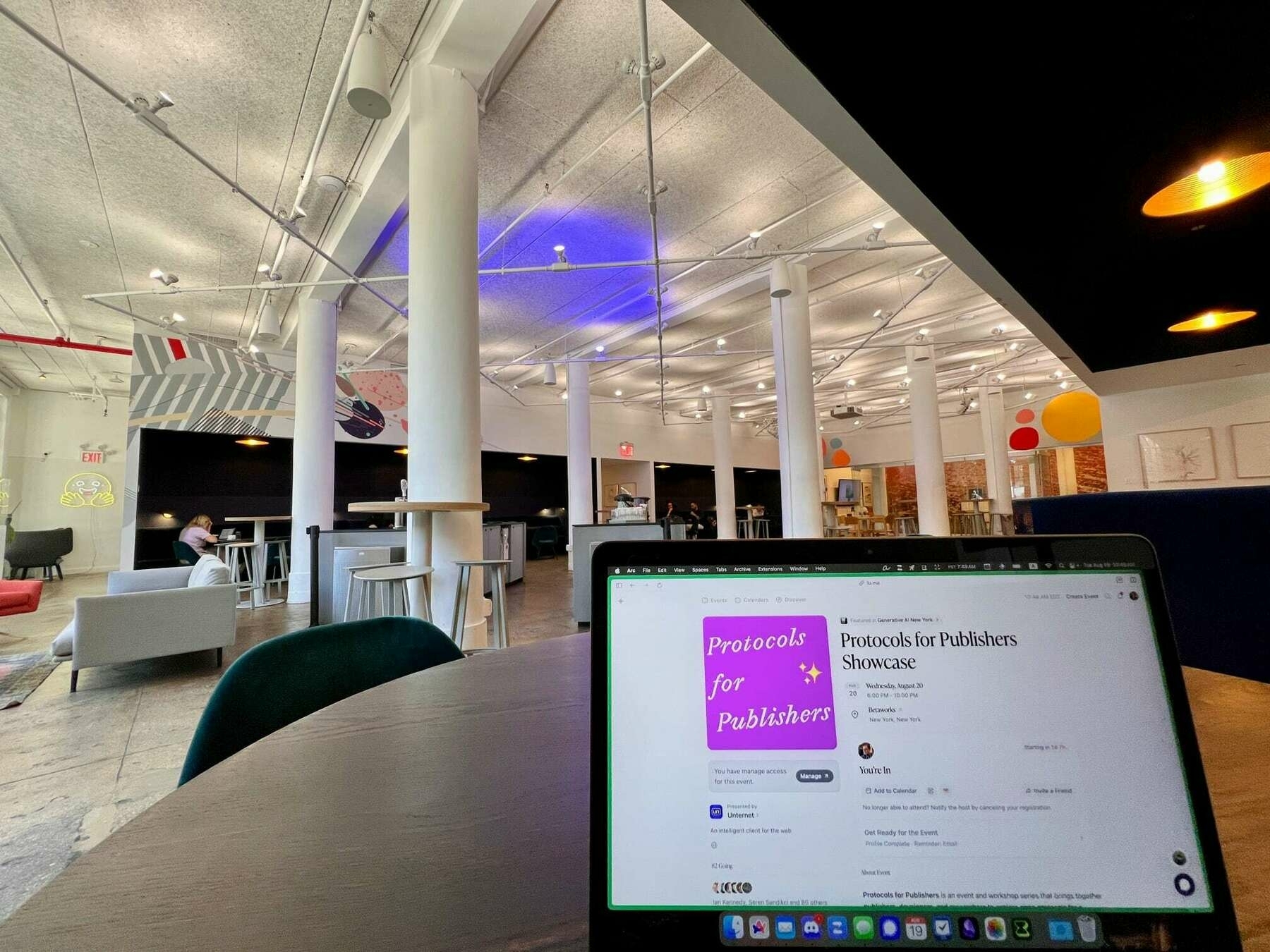 Wide angle interior of a large bright room with many tables and chairs. In the foreground is a MacBook with the Luma event for Protocols for Publishers displayed