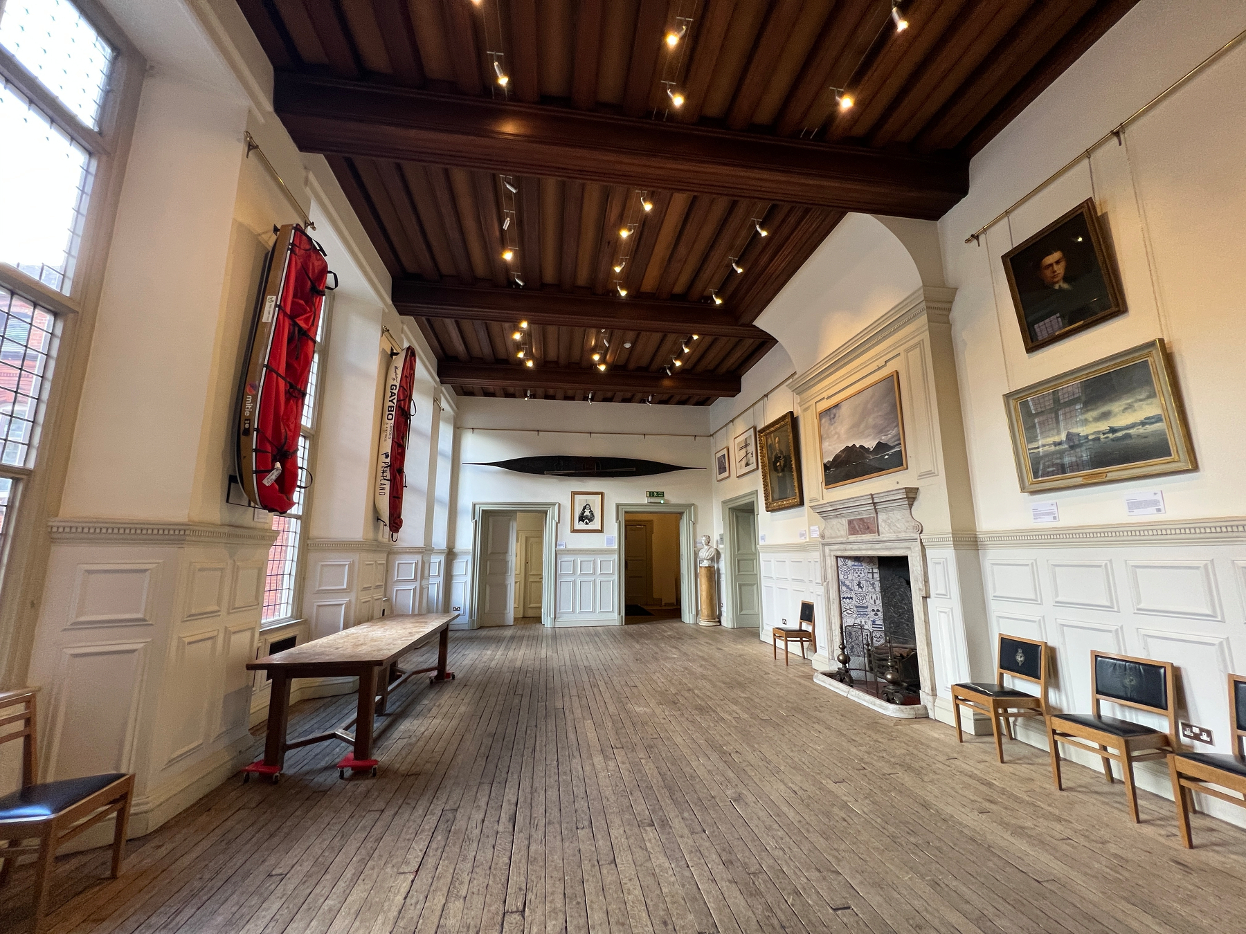 One of the large rooms of the RGS with high ceilings and a bare wooden floor, pictures of explorers and kayaks hanging off the walls. 