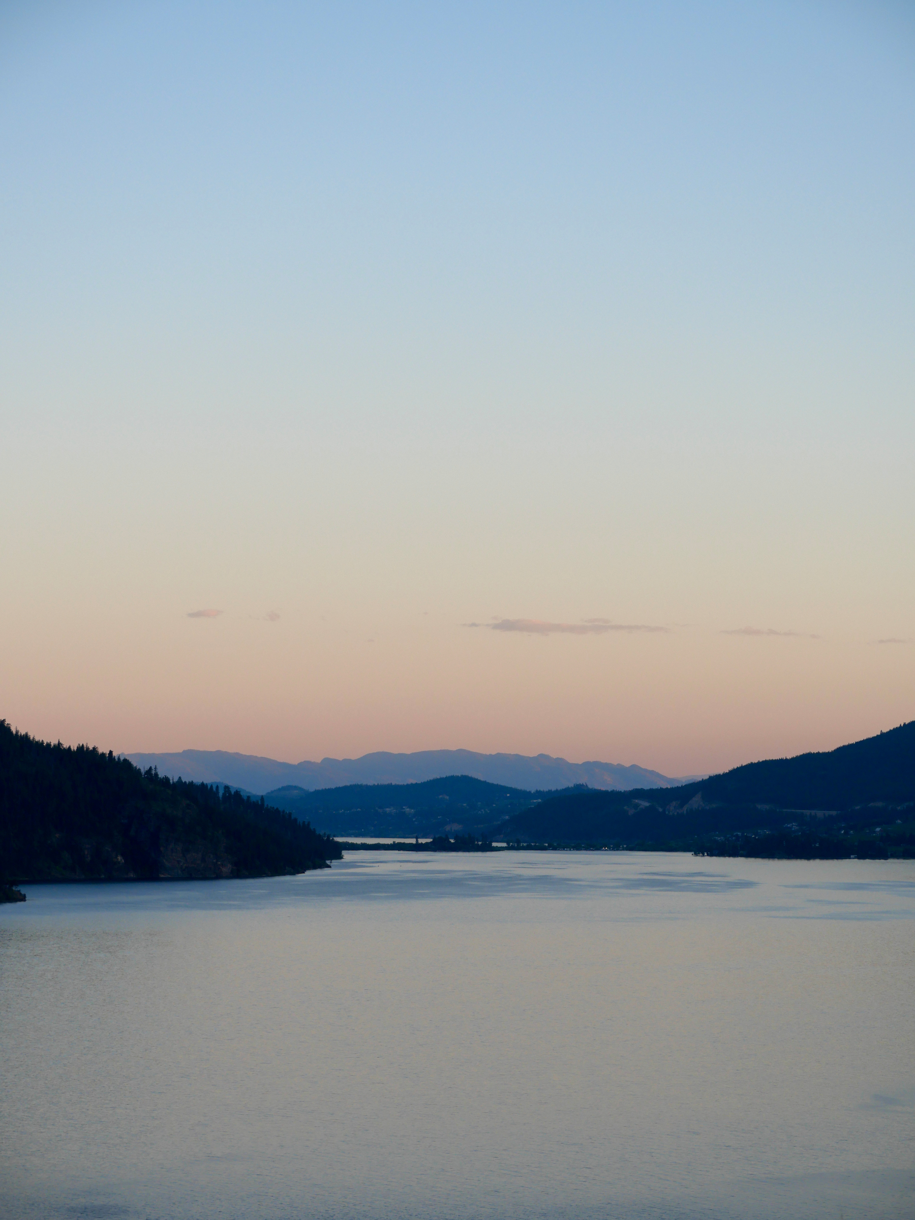 Sun sets over Oyama BC on Okanagan Lake. Sky is a clear peach and salmon gradient with a single strand of thin cloud 