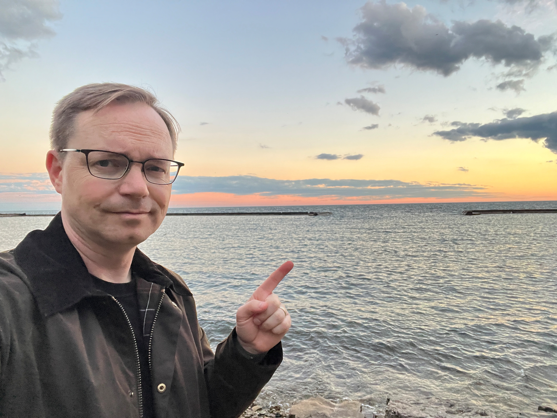 Chad selfie pointing towards the horizon over a body of water at sunset.
