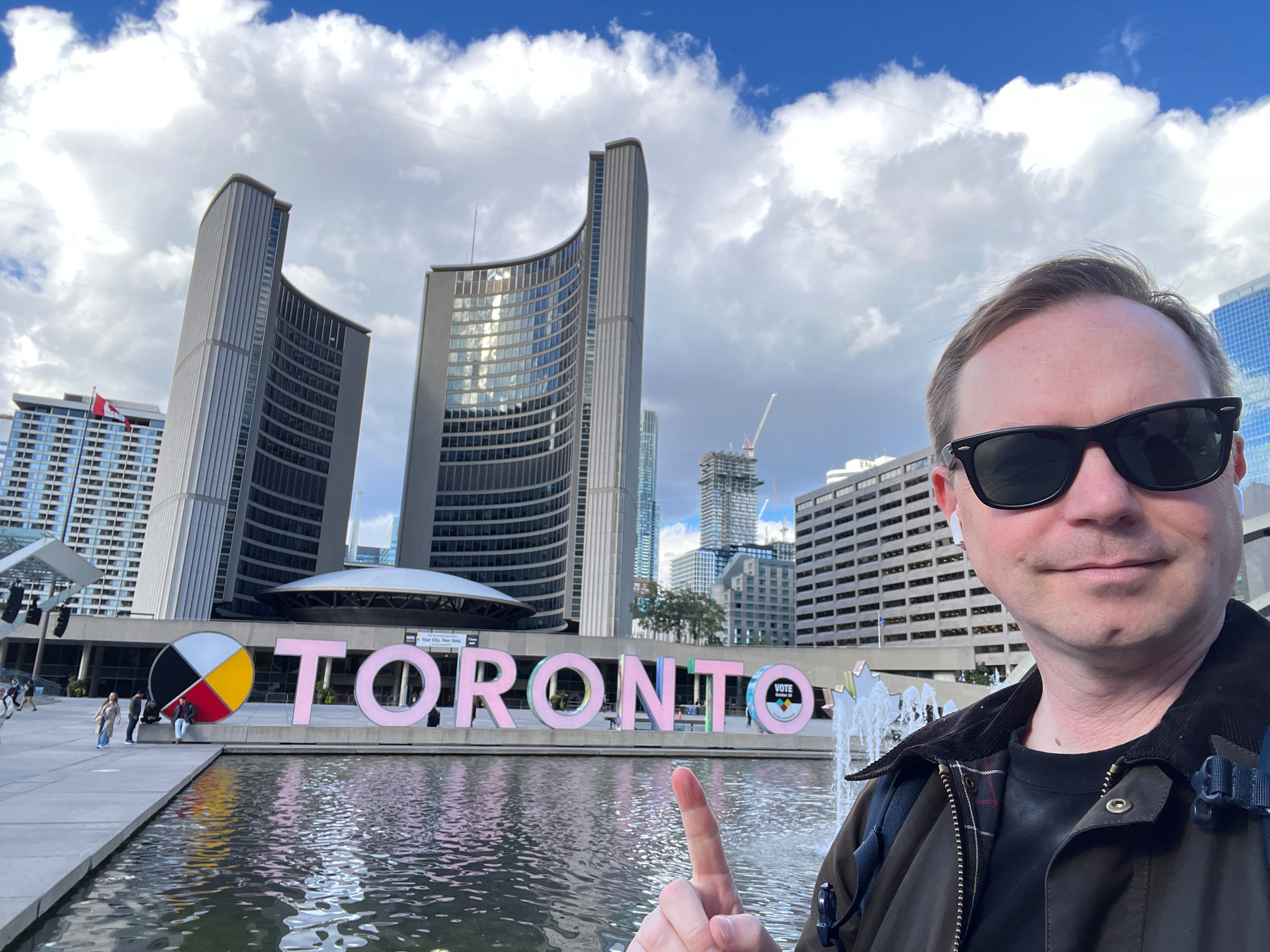 Chad selfie in front of the colorful Toronto sign with City Hall and some epic anime clouds in the background.