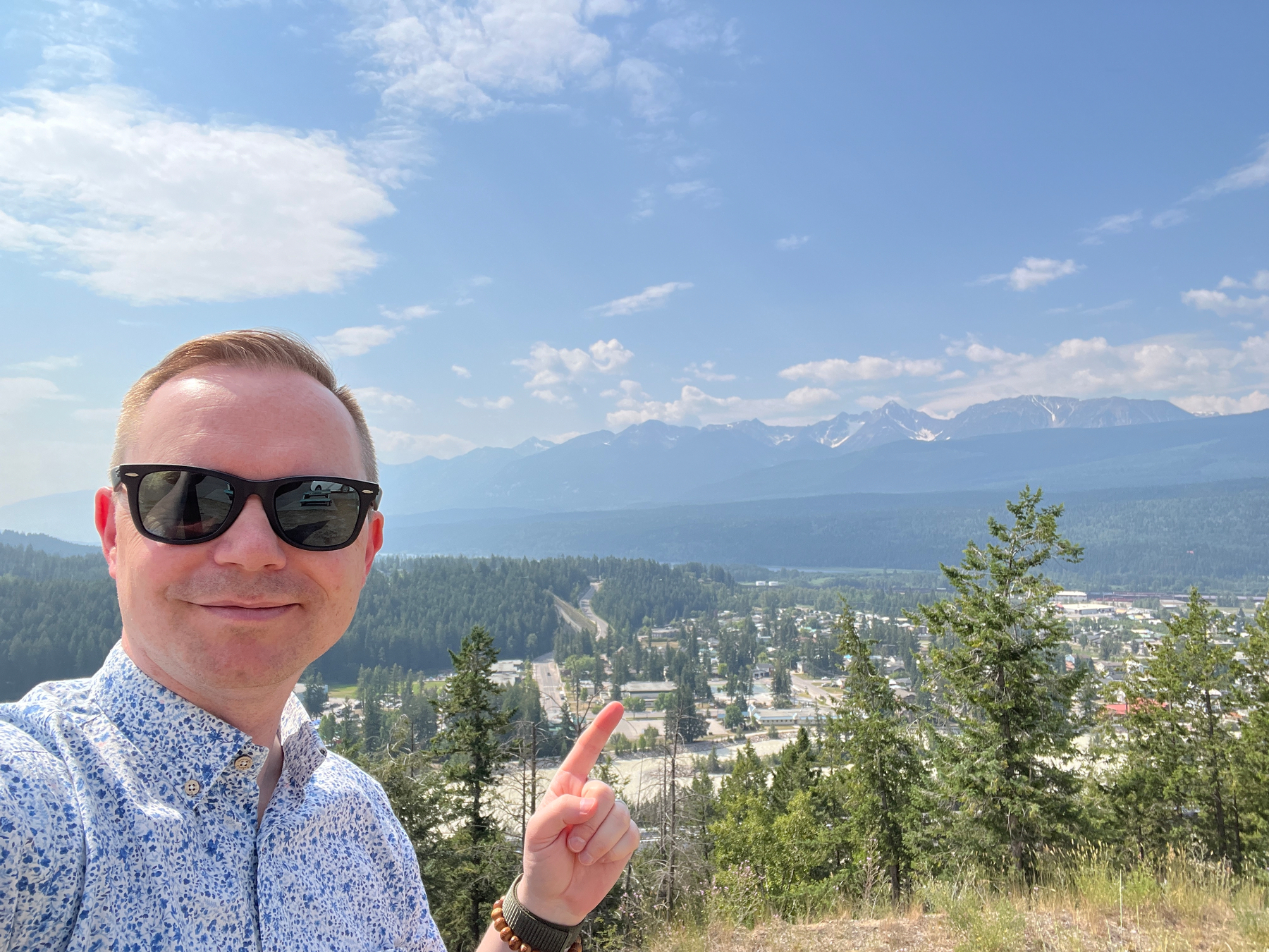 Chad selfie at a viewpoint over a small town with large mountains in the background (with visible snow)