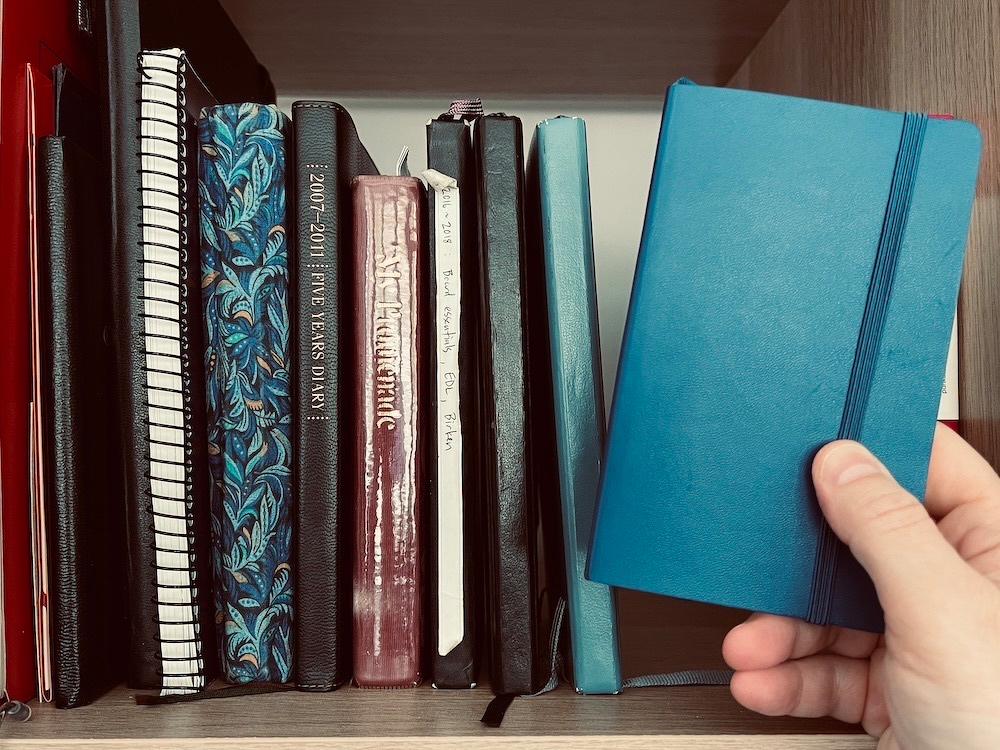 A shelf of journals with Chad holding a small blue pocket notebook