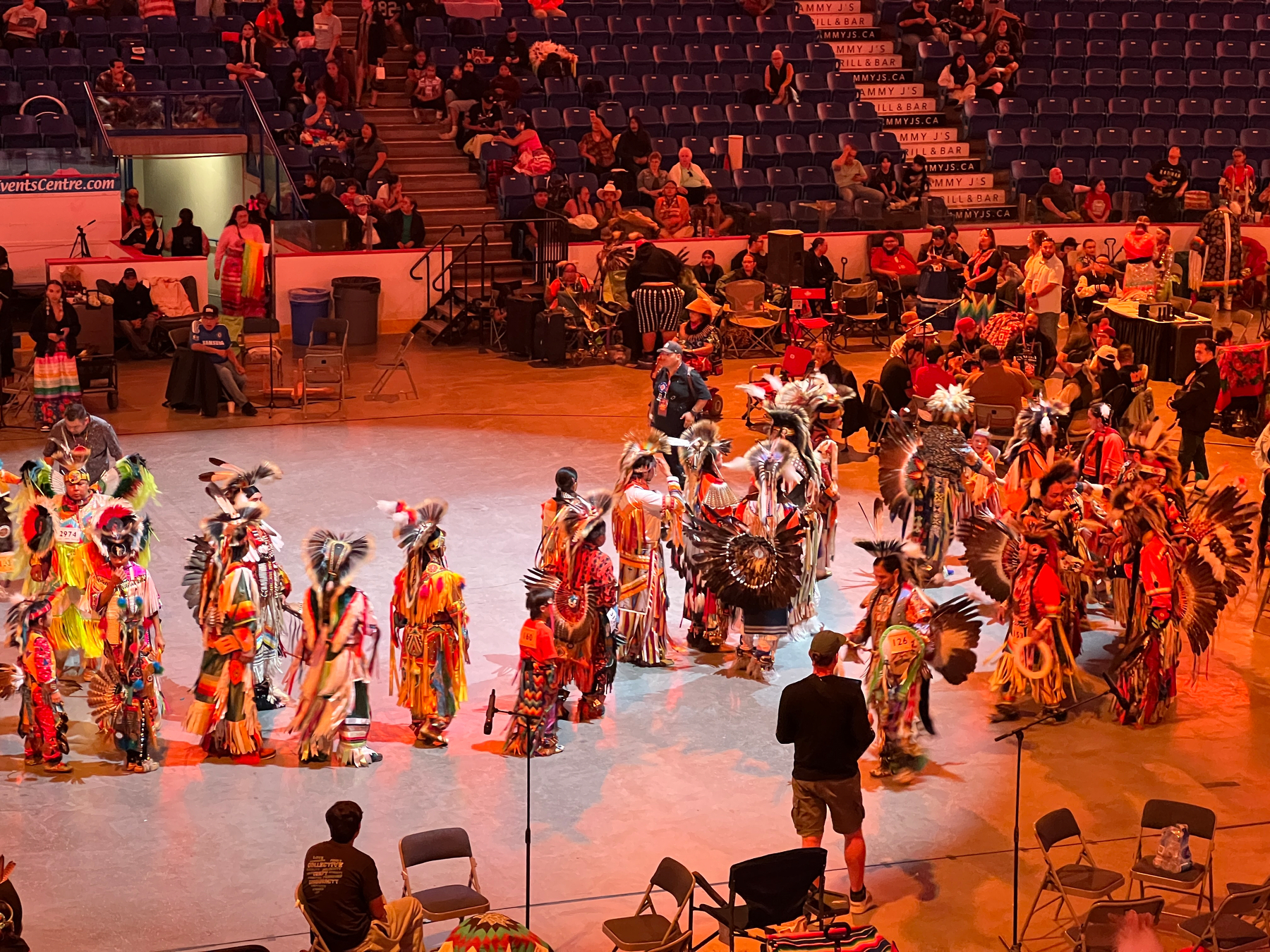 A group of people dressed in vibrant traditional indigenous regalia line up to shake hands with the winners of the dance contest