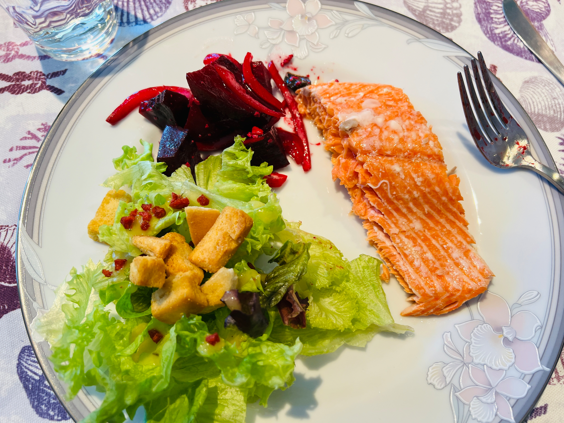 Dinner plate with a chunk of salmon fillet, red beet salad, and a green salad with croutons 