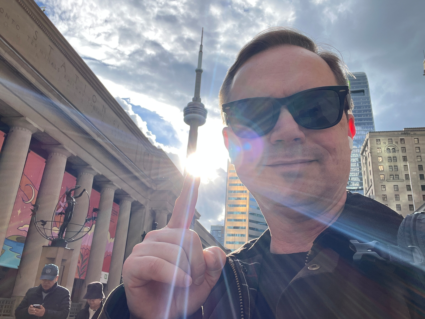 Chad selfie with the CN Tower.  Sun shines from behind the tower right where Chad is pointing
