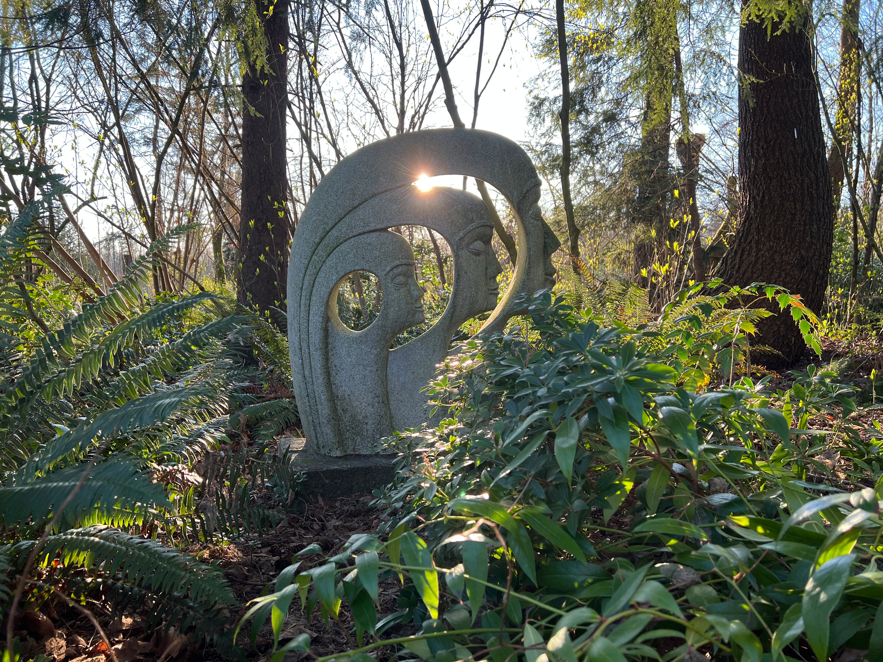 Sculpture of three faces backlit by a low sun